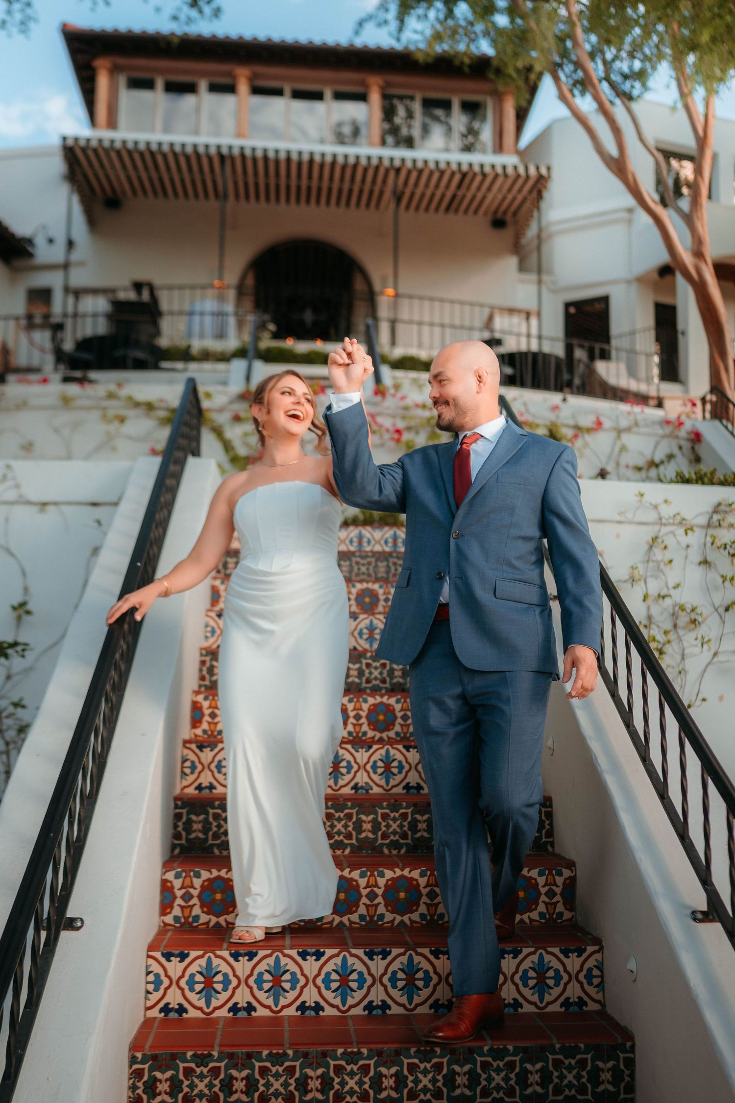Joyful bride and groom descend colorful tiled stairs hand in hand at wedding venue.