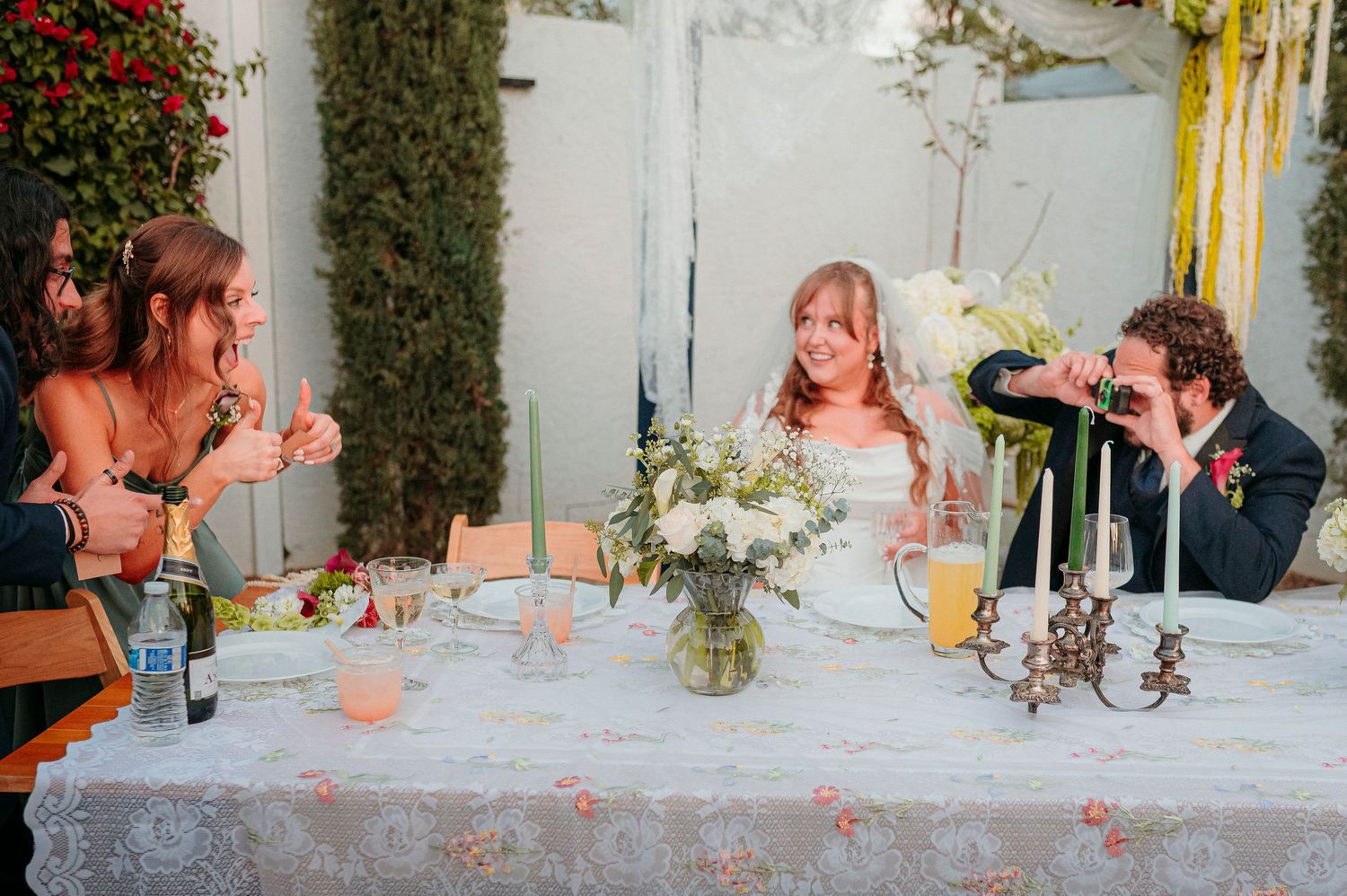 Bride and groom sharing a fun moment at sweetheart table during outdoor wedding reception dinner.