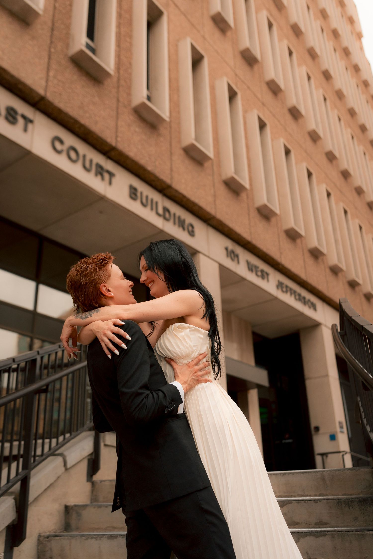 Newlyweds embrace and laugh together on steps of Phoenix West Jefferson Court Building.