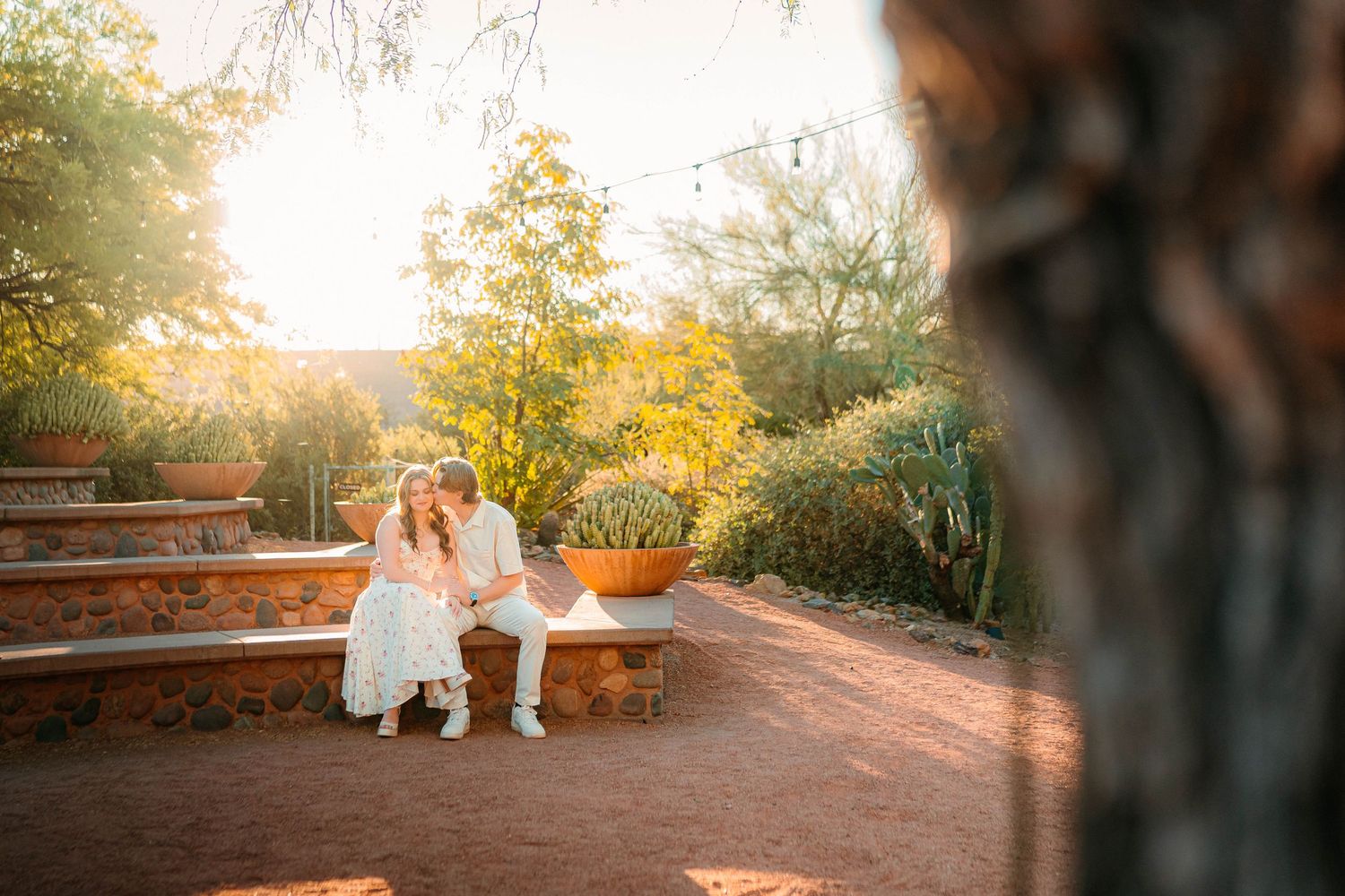 Couple shares a romantic moment on stone steps surrounded by lush desert garden at golden hour wedding.