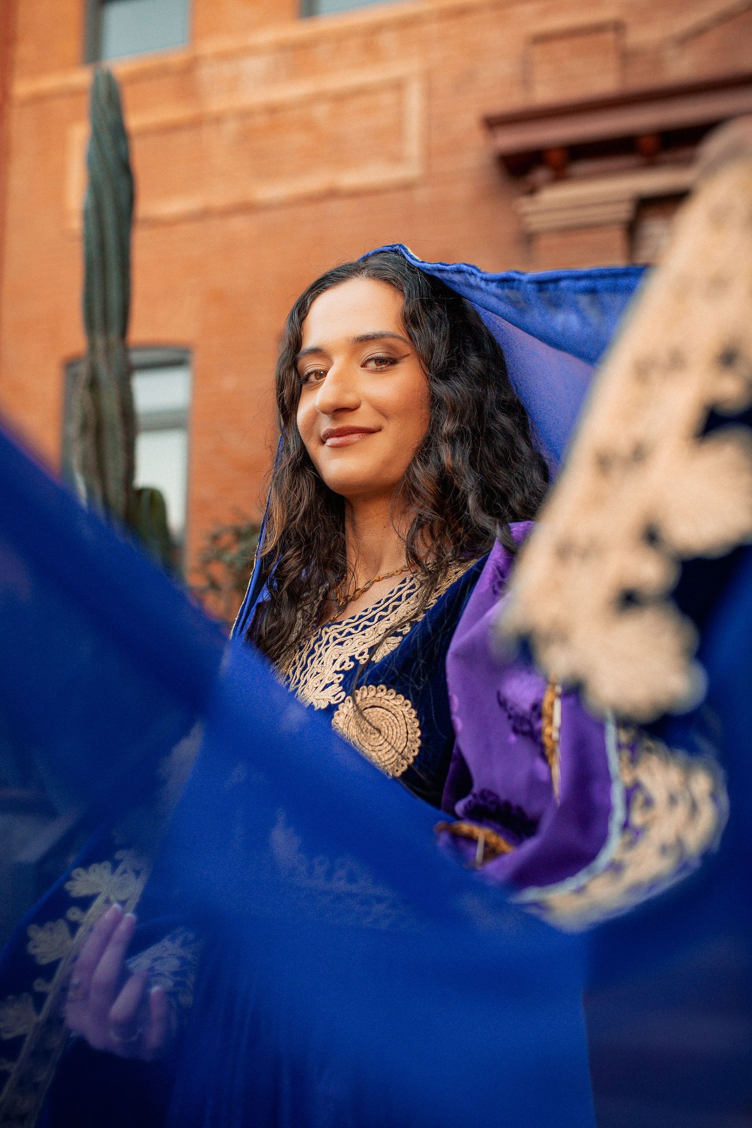 A woman in ornate blue traditional attire smiles surrounded by flowing blue fabric.