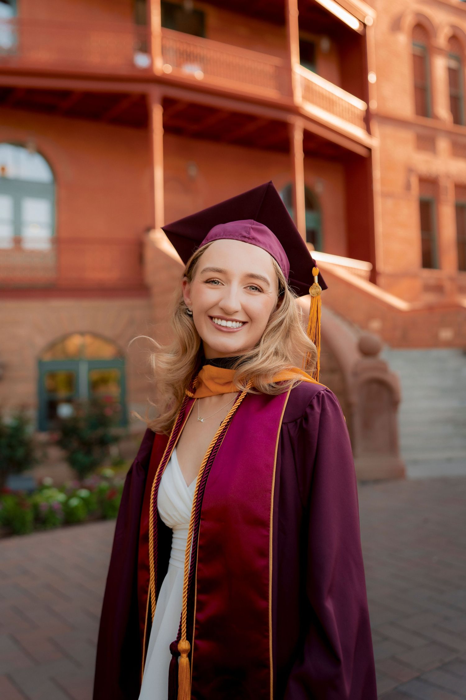 Smiling graduate in maroon cap and gown with gold honor cord at ASU campus.