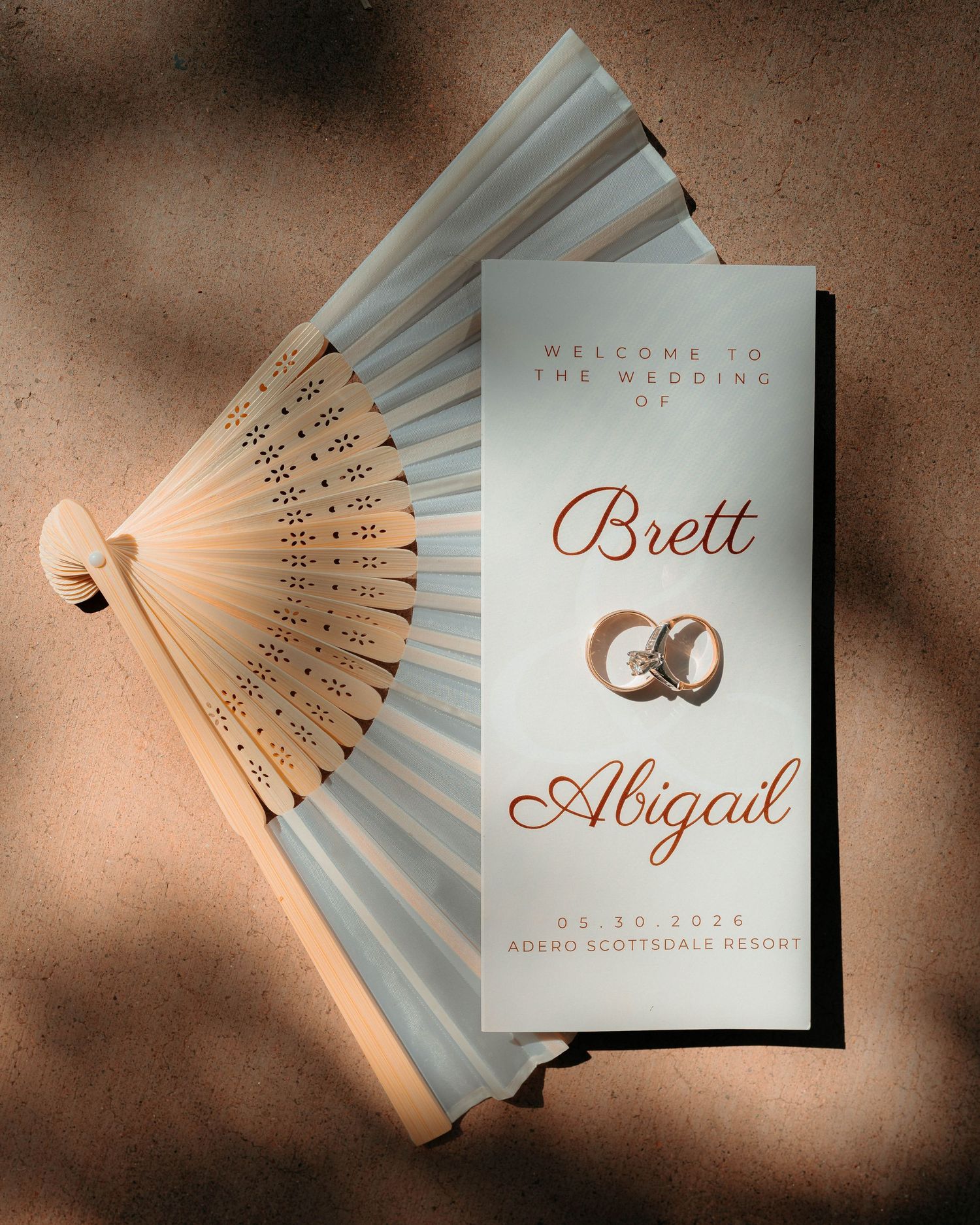 Elegant wedding program for Brett and Abigail at Adero Scottsdale Resort displayed with a decorative hand fan.