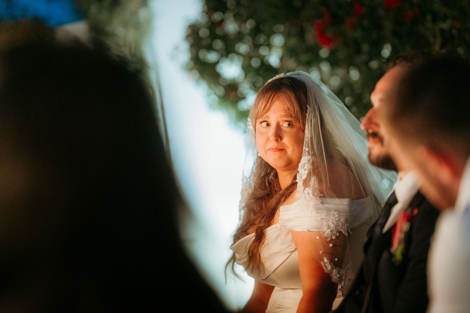 Emotional bride in pearl-trimmed veil gazing at groom during outdoor wedding ceremony.