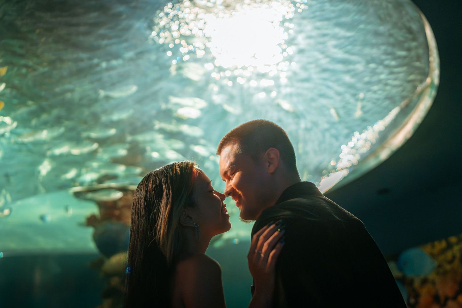 Romantic couple sharing an intimate moment in front of a glowing aquarium tank with fish swimming overhead.