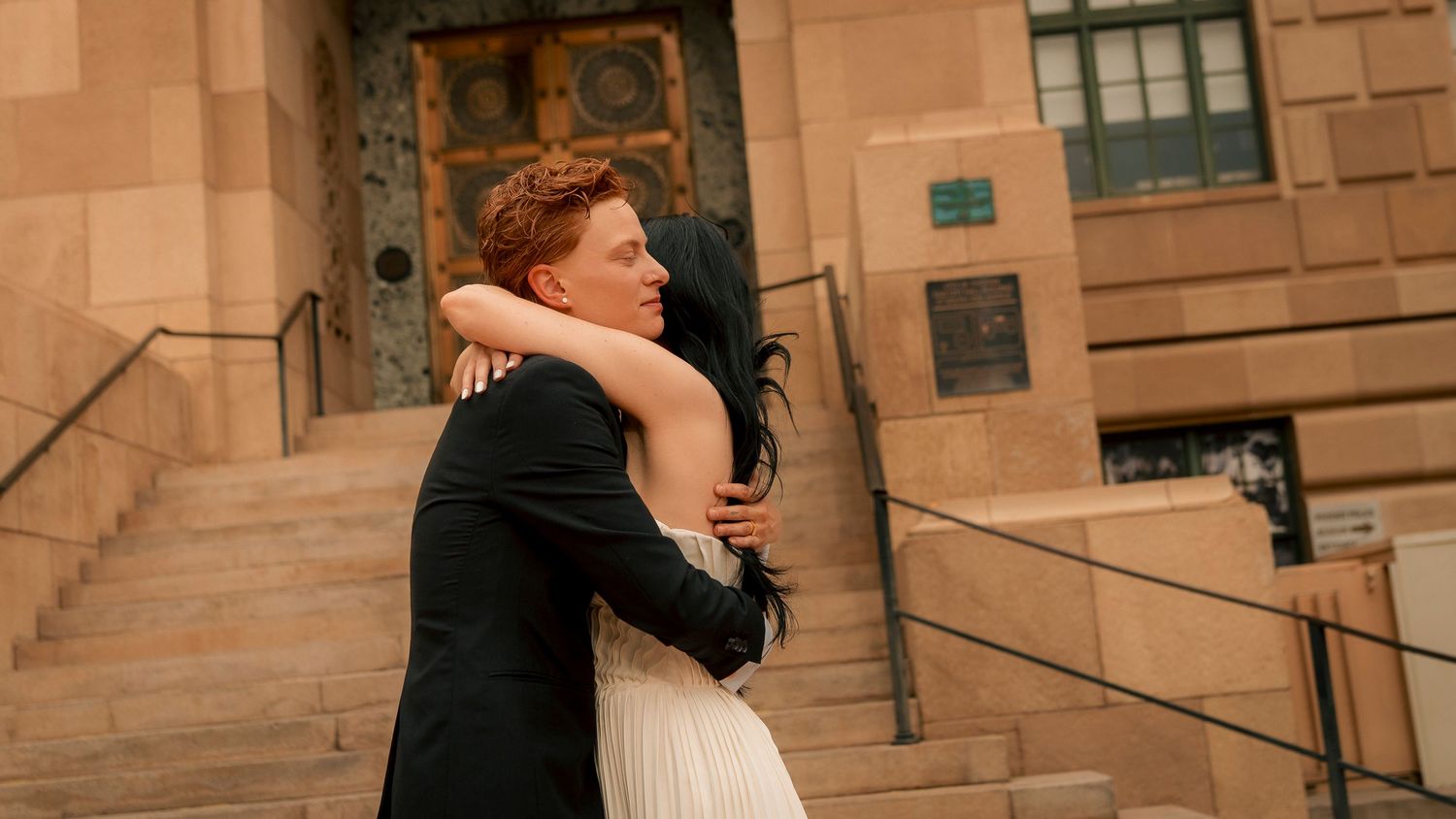 Couple embracing in a tender hug outside a historic stone building, bride in white dress and groom in dark suit.