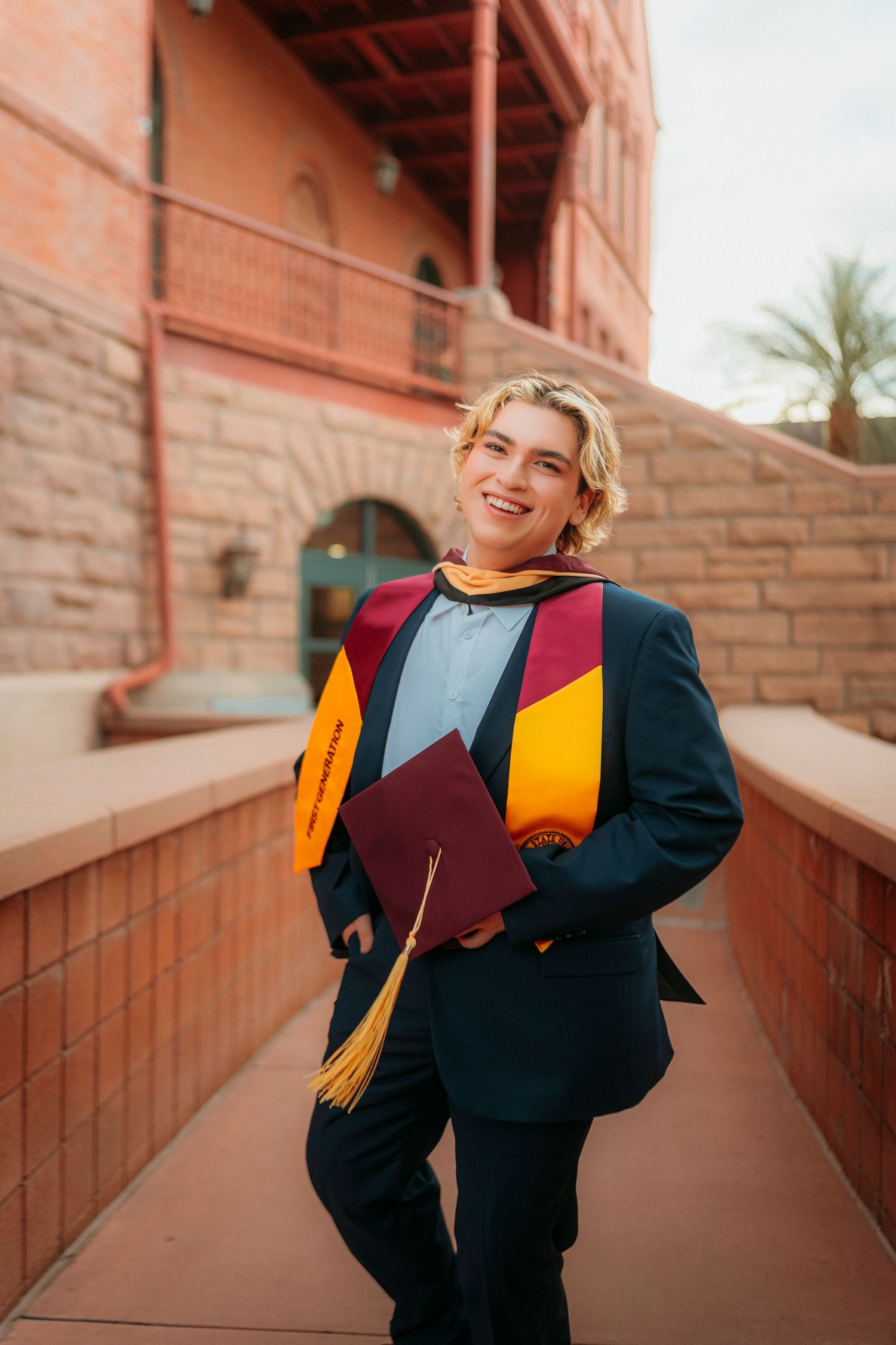 Smiling graduate in navy blazer holding maroon cap with gold tassel at ASU campus.