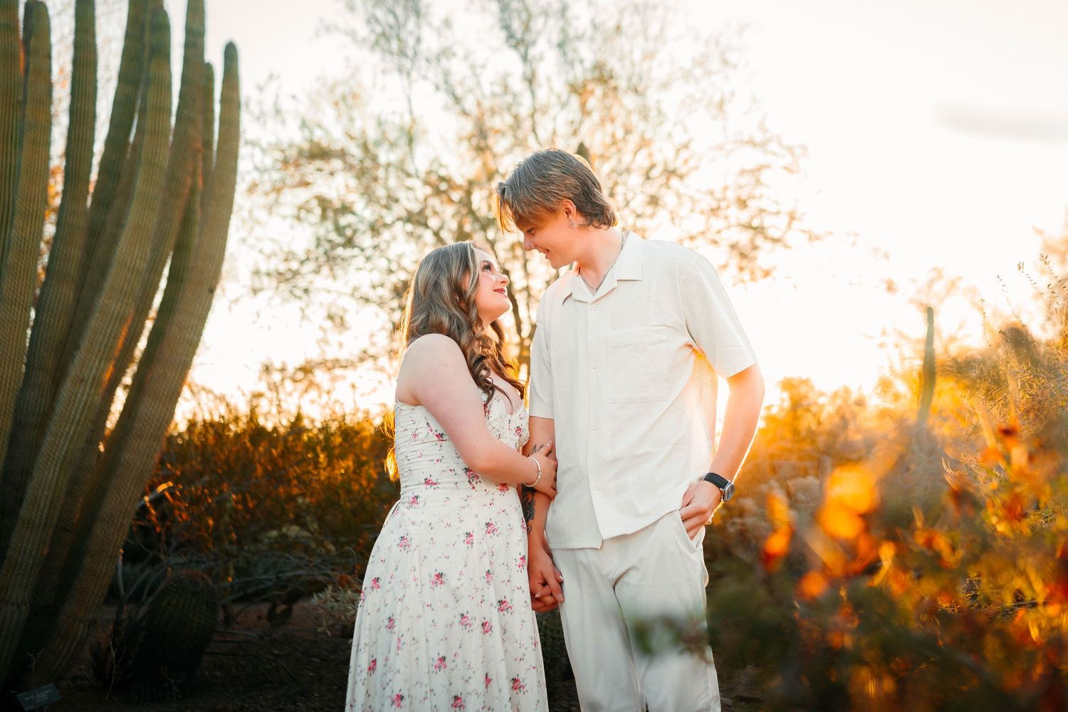 Couple sharing a romantic moment at golden hour in a desert garden with saguaro cacti and warm sunset light.