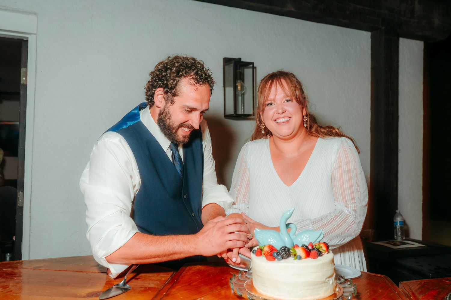 Bride and groom cutting their white wedding cake decorated with fresh strawberries together at their reception.