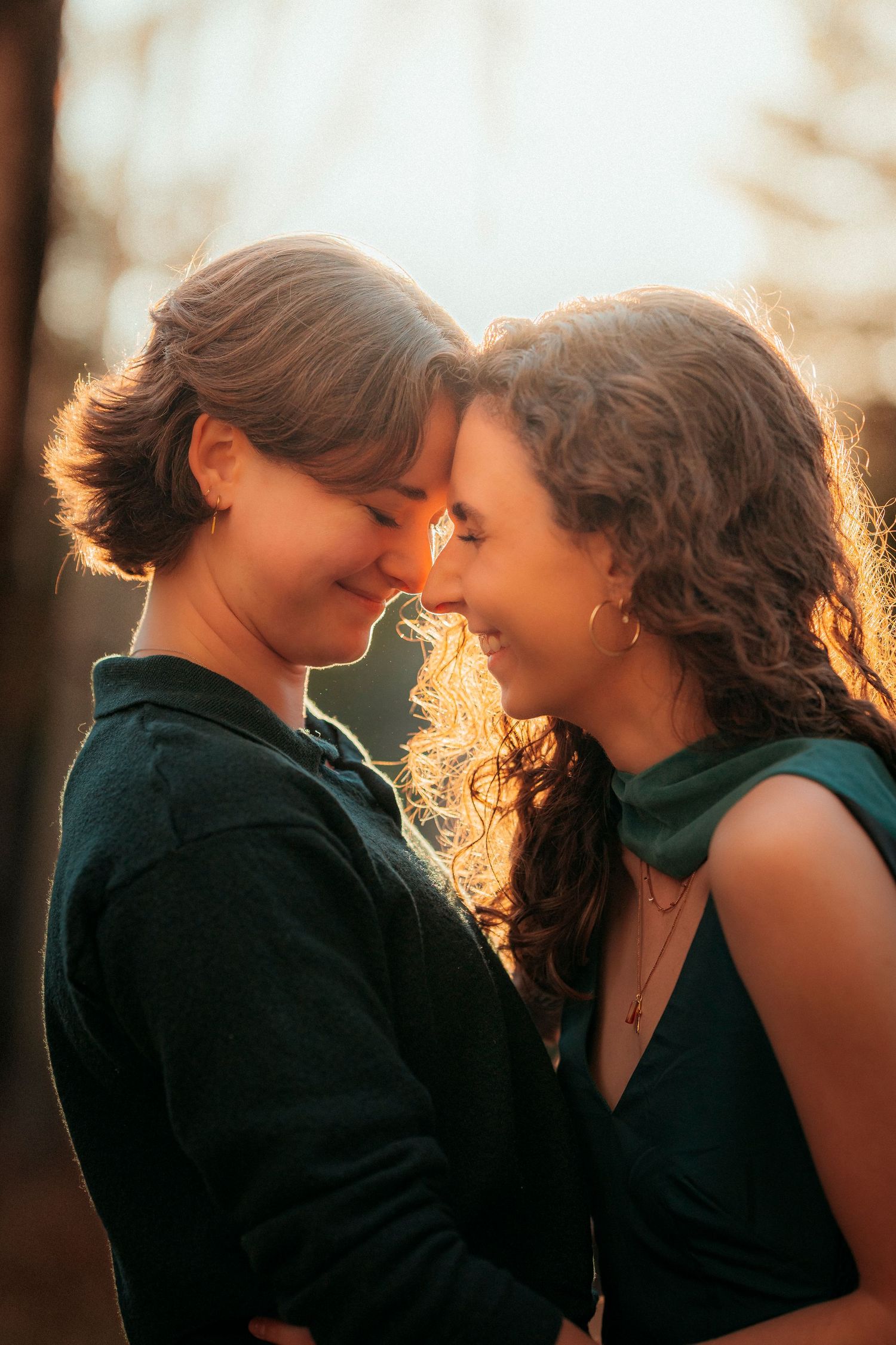 Two women share tender forehead touch moment bathed in warm golden sunset backlight.