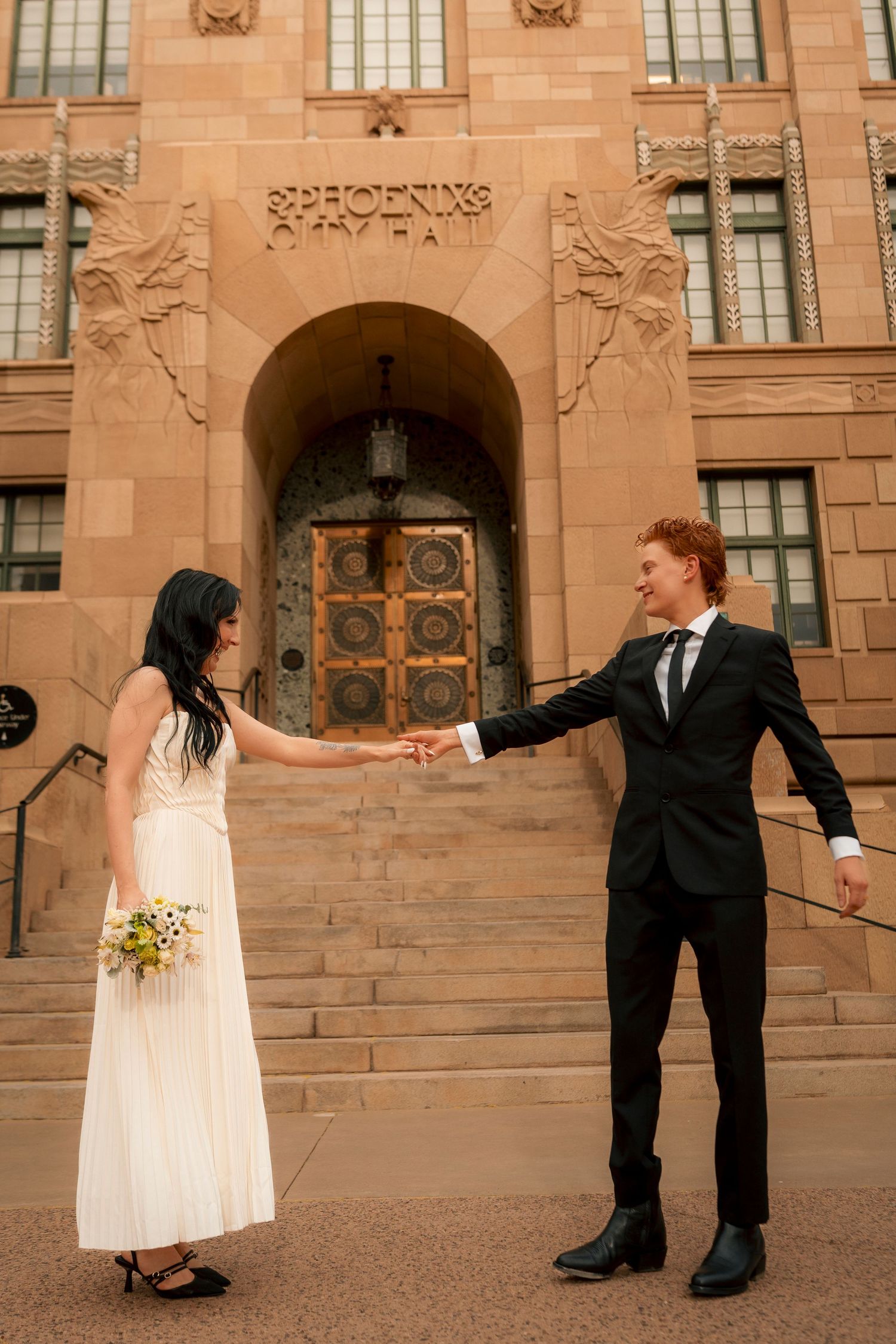 Smiling newlyweds hold hands outside Phoenix City Hall after their wedding ceremony.