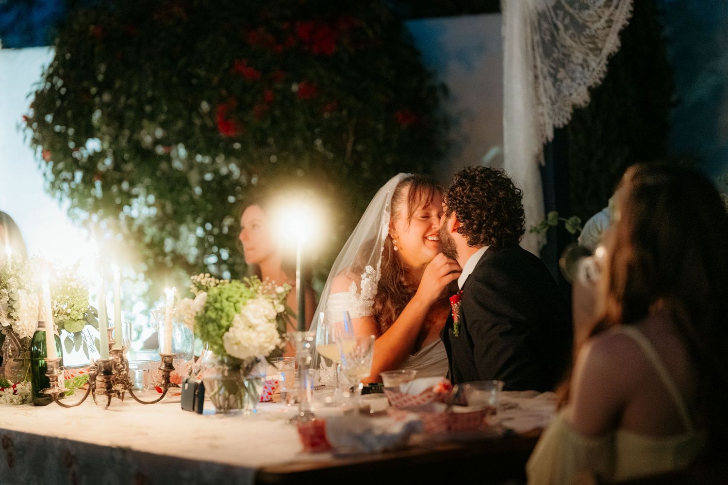 Newlyweds sharing a romantic kiss at candlelit wedding reception dinner table.