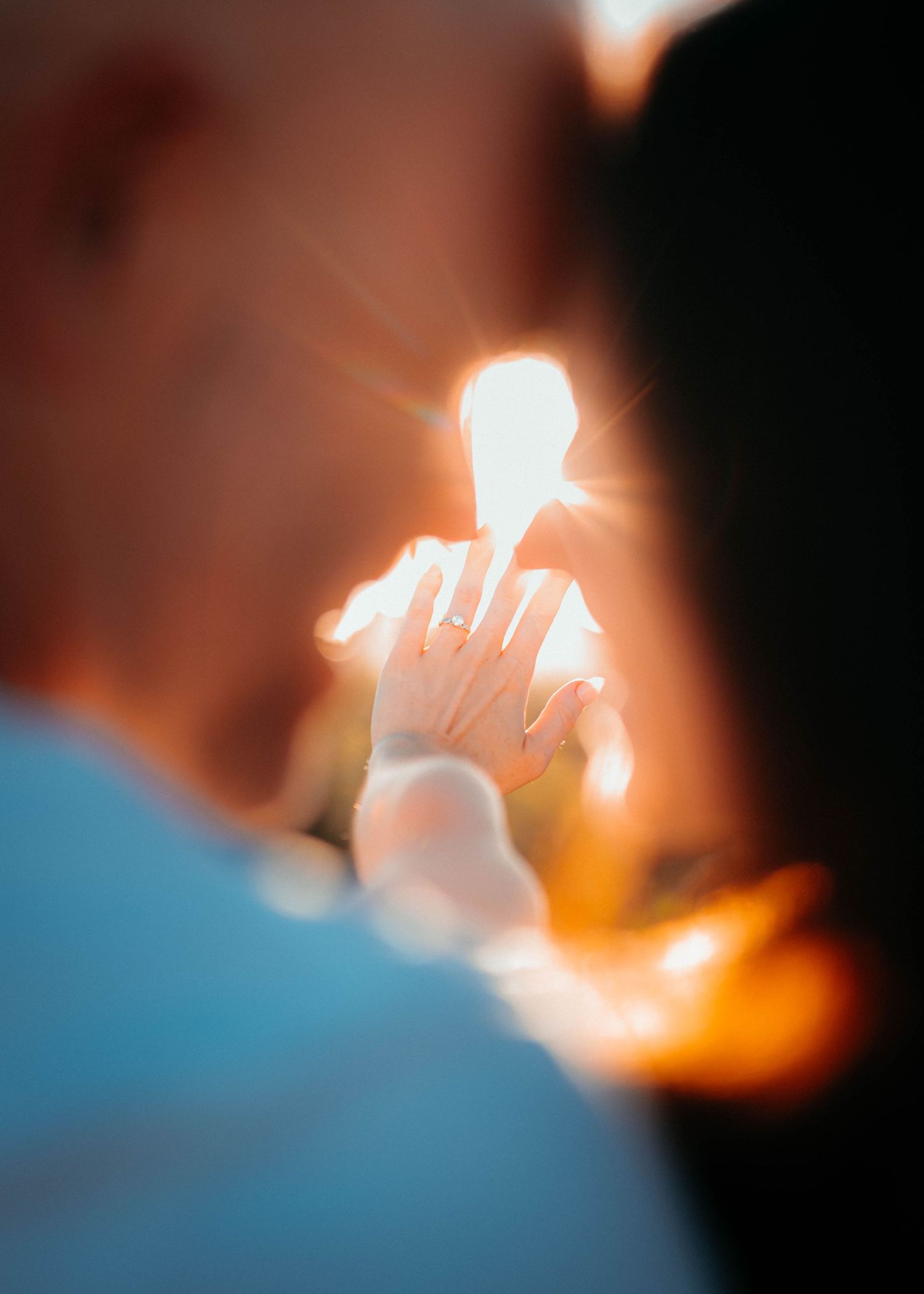 Couple holding hands with engagement ring glowing in golden sunlight during romantic outdoor proposal moment.