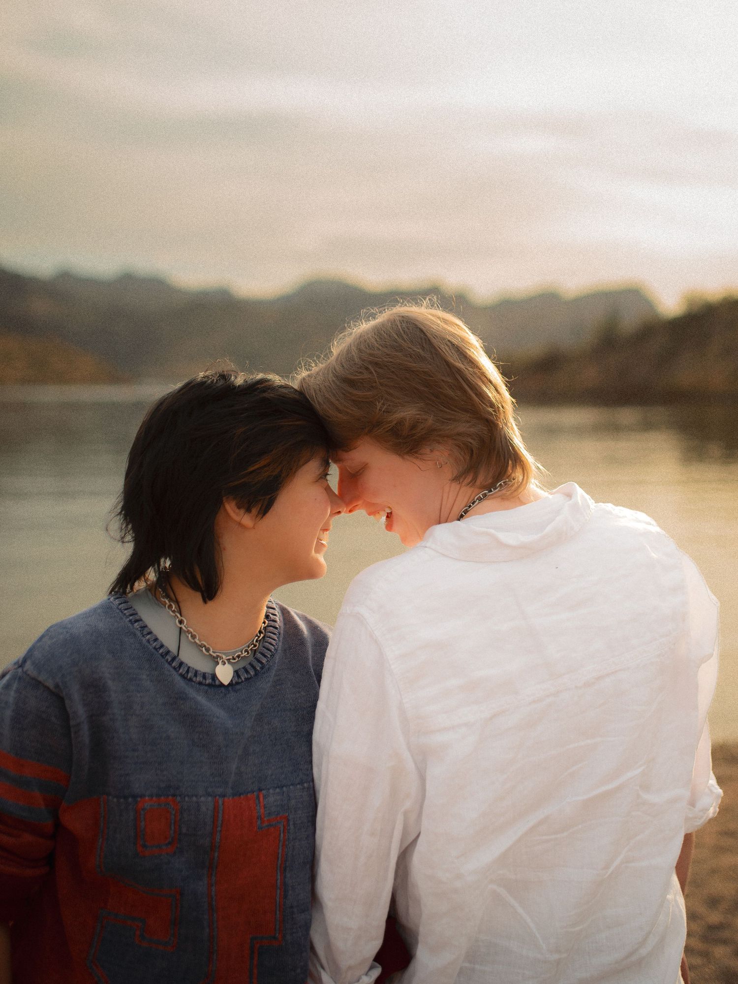 Romantic couple touching foreheads tenderly by a serene lake at warm golden sunset.