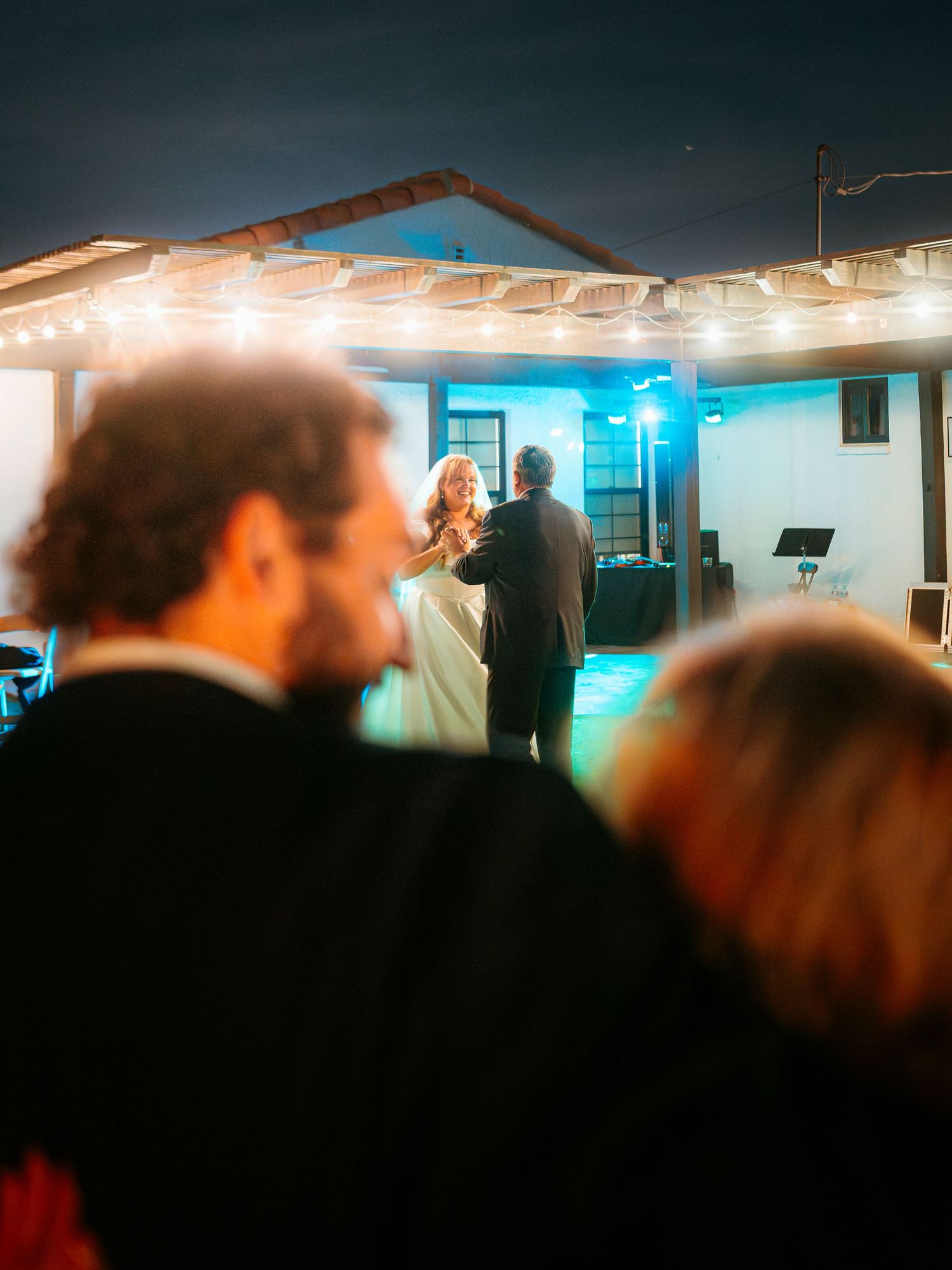 Guests watch a couple share their first dance under string lights at an outdoor evening wedding reception.