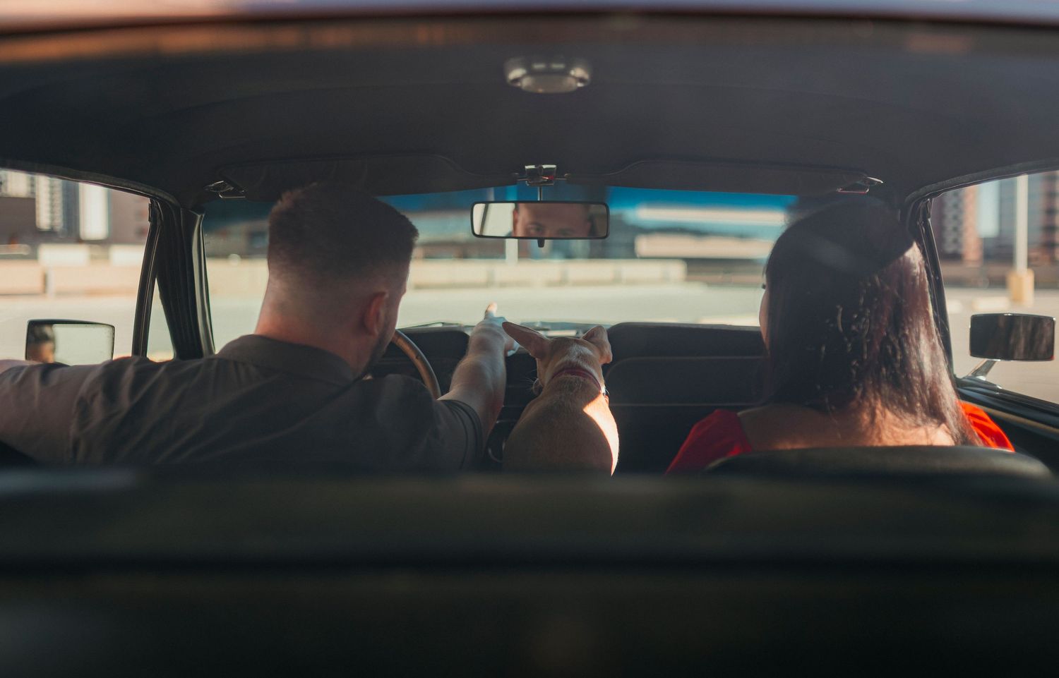 Couple sitting in the back seat of a vintage car, viewed from behind, sharing an intimate moment.