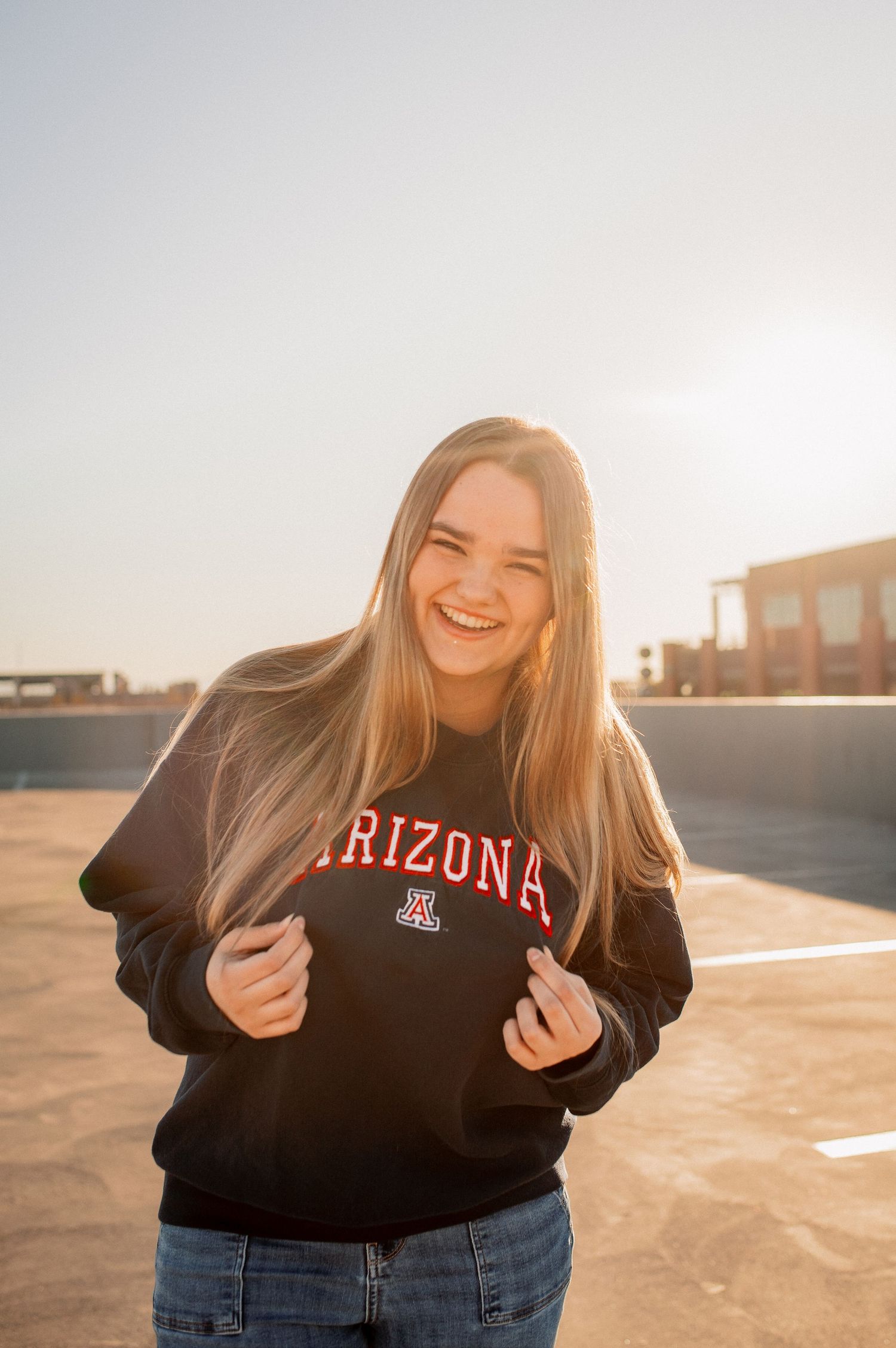 Happy young woman laughing in University of Arizona black sweatshirt in golden sunlight.