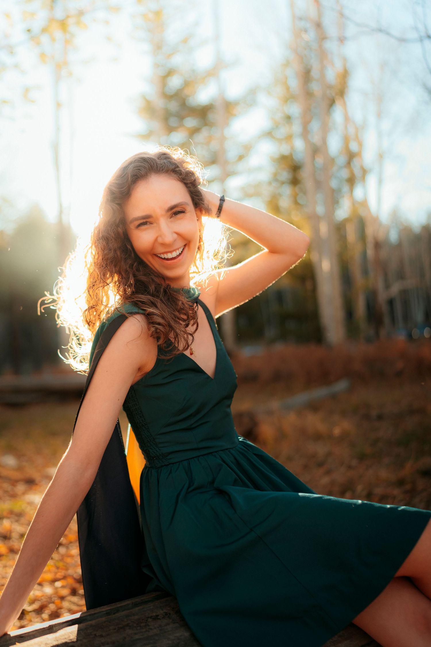 Happy young woman in green dress sitting outdoors in autumn sunlight with curly hair.