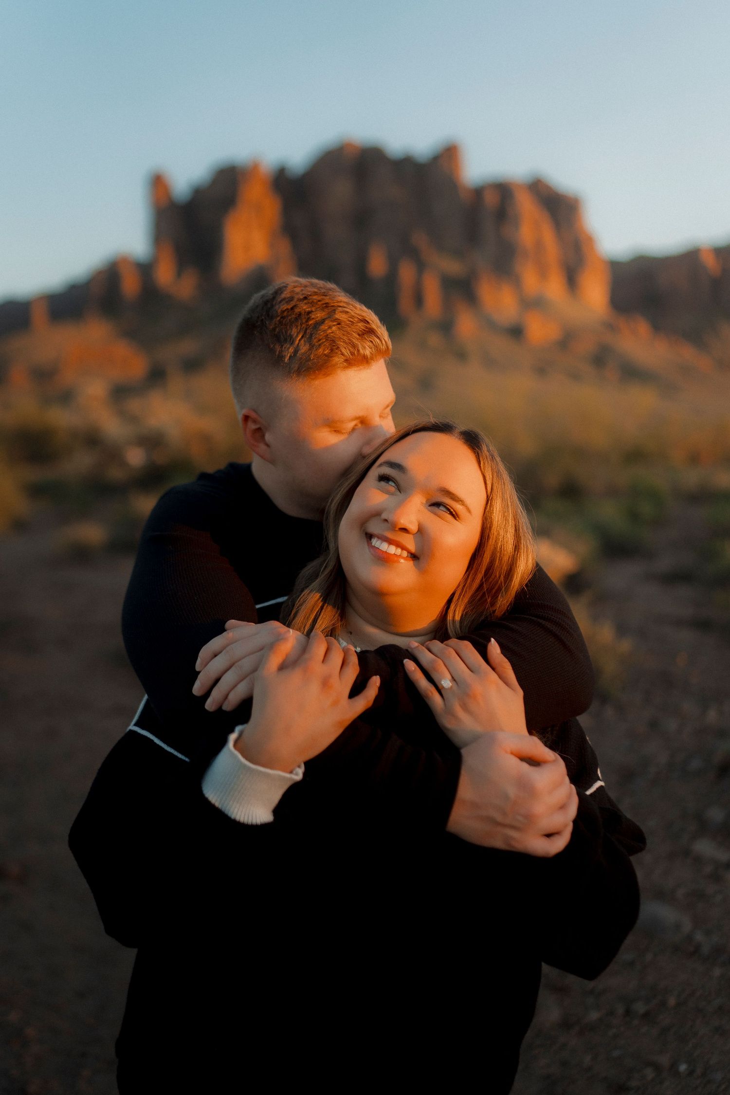 Happy couple embracing at sunset with dramatic Superstition Mountains in the background.