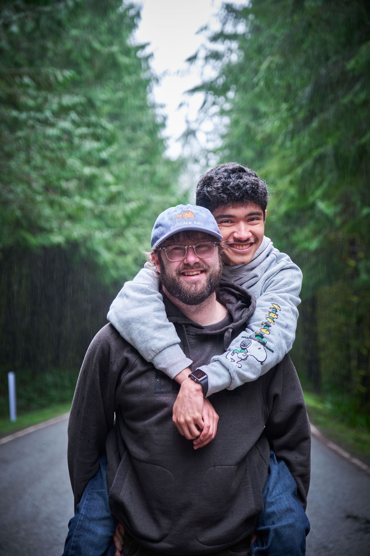A couple, one of them is giving a piggyback ride to the other in a WA, State forest in the rain. Photo by N&D Wedding Photography and Film