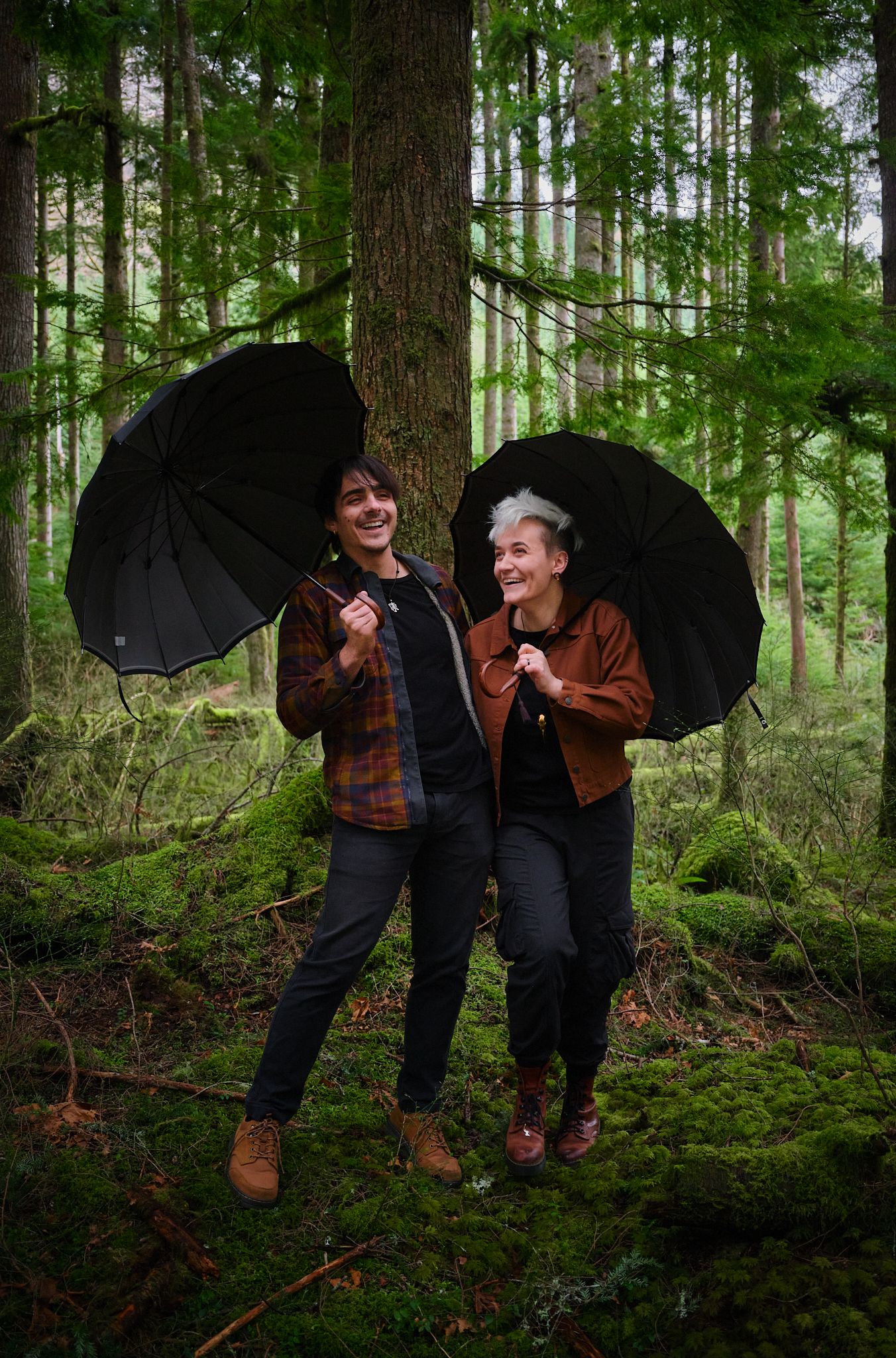 A couple laughing while holding umbrellas in a forest in Washington State. Photo by N&D Wedding Photography and Film