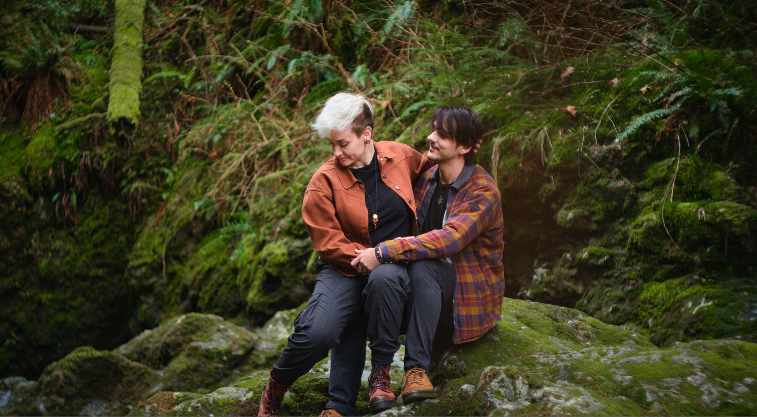 A couple sitting on a mossy boulder in a forest in Washington State. Photo by N&D Wedding Photography and Film