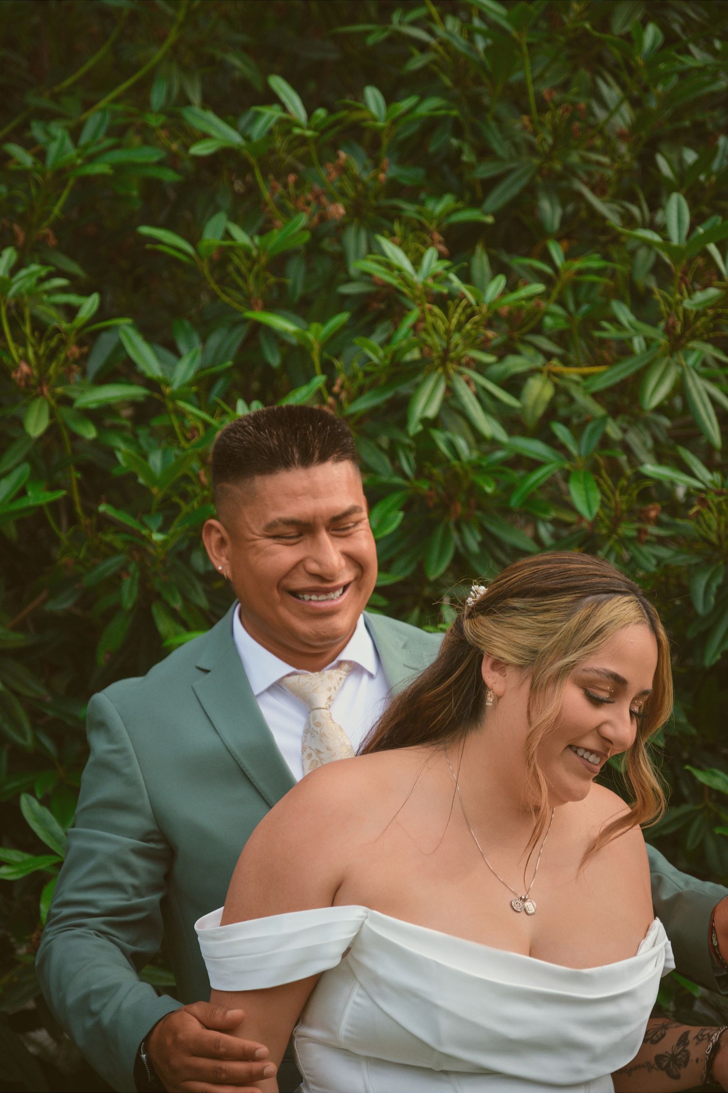 A married couple laughing outside by the bushes in Tulalip Washington. Photo by N&D Wedding Photography and Film