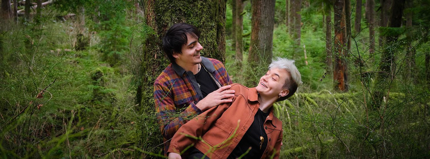 A couple acting silly while leaning against a tree in a forest in Washington State. Photo by N&D Wedding Photography and Film