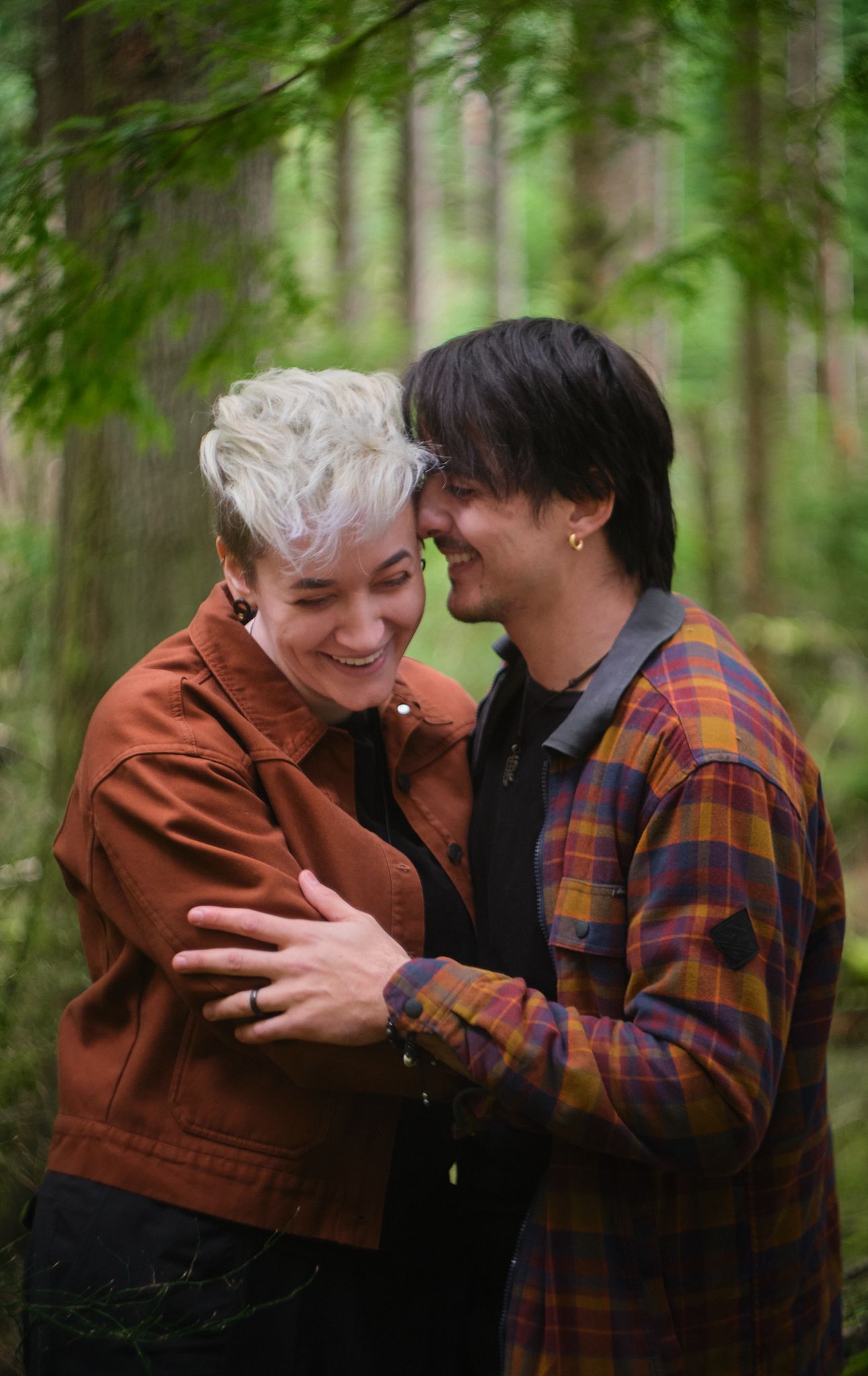 A couple giggling while embracing in a dense forest in Washington State. Photo by N&D Wedding Photography and Film