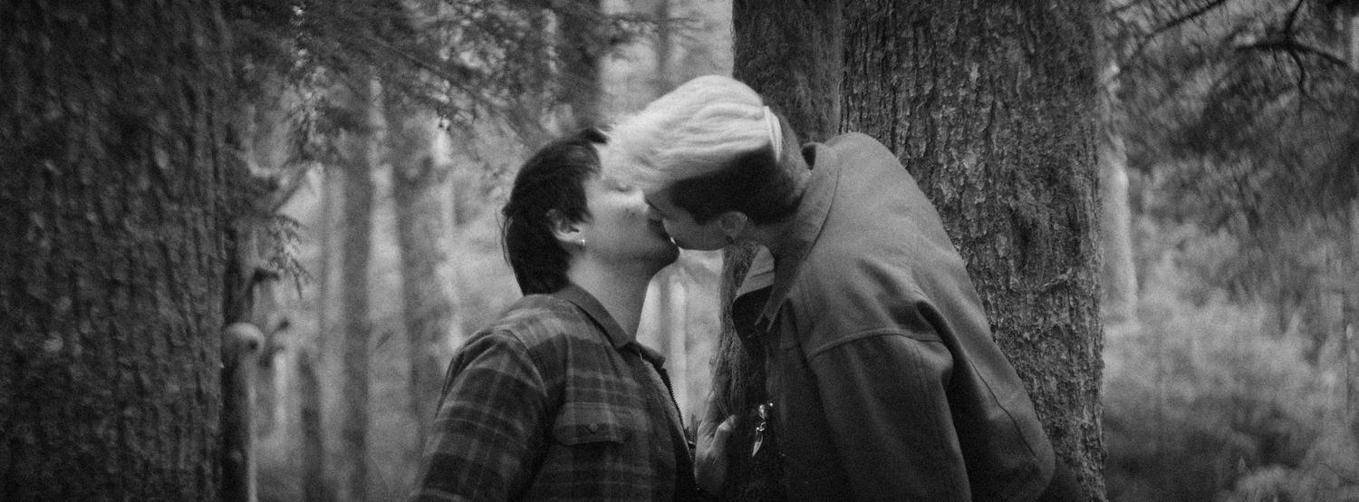 A vintage style photo of couple kissing and leaning on a tree in a forest in Washington State. Photo by N&D Wedding Photography and Film