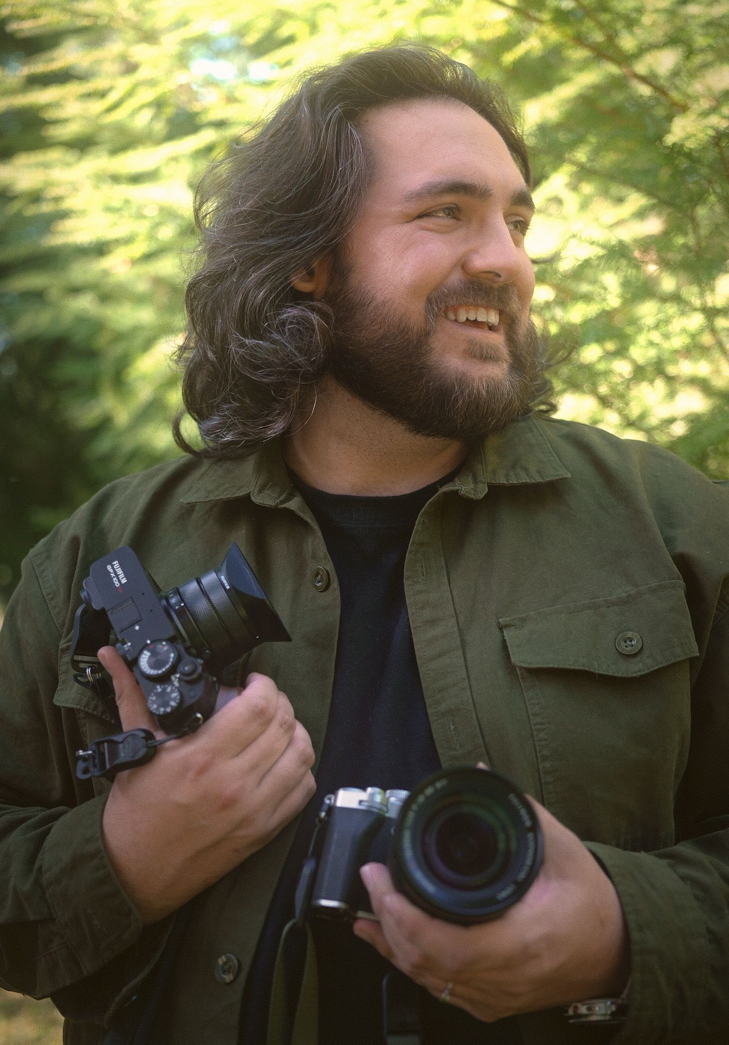 Dawson the photographer for N&D Wedding Photography and Film holding his GFX 100RF and X-T5 cameras in a forest in Washington State.