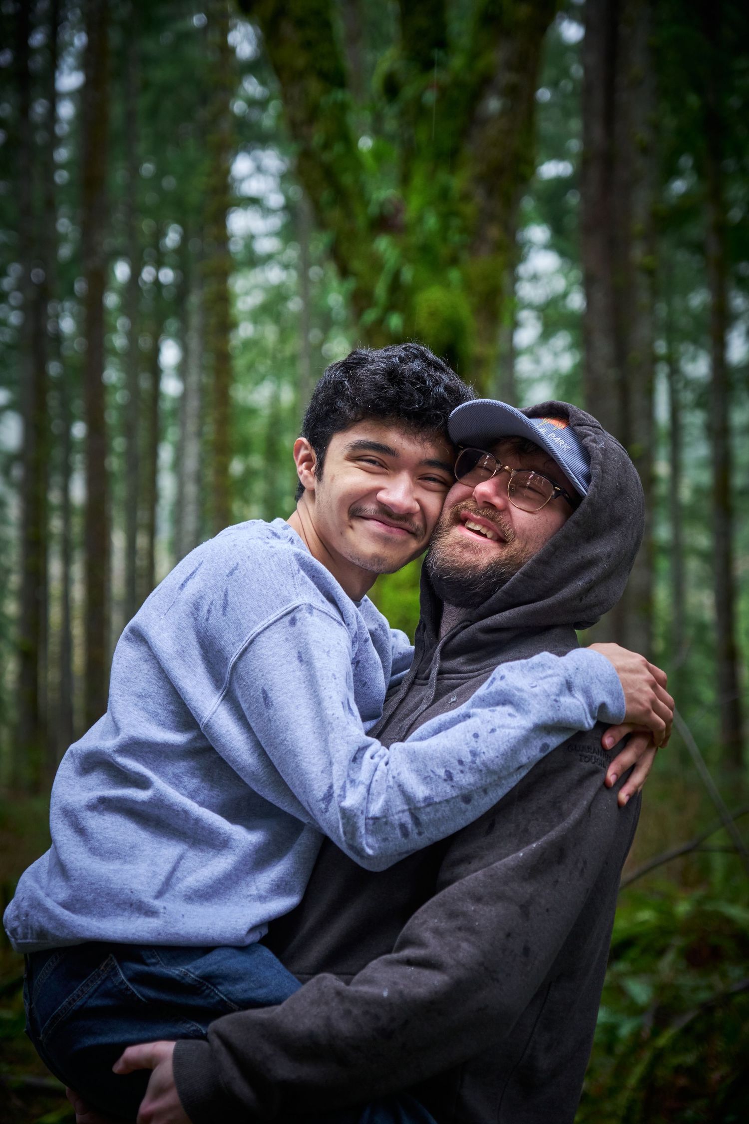 A couple embracing in a Washington State forest in the rain, one of them is carrying the other. Photo by N&D Wedding Photography and Film
