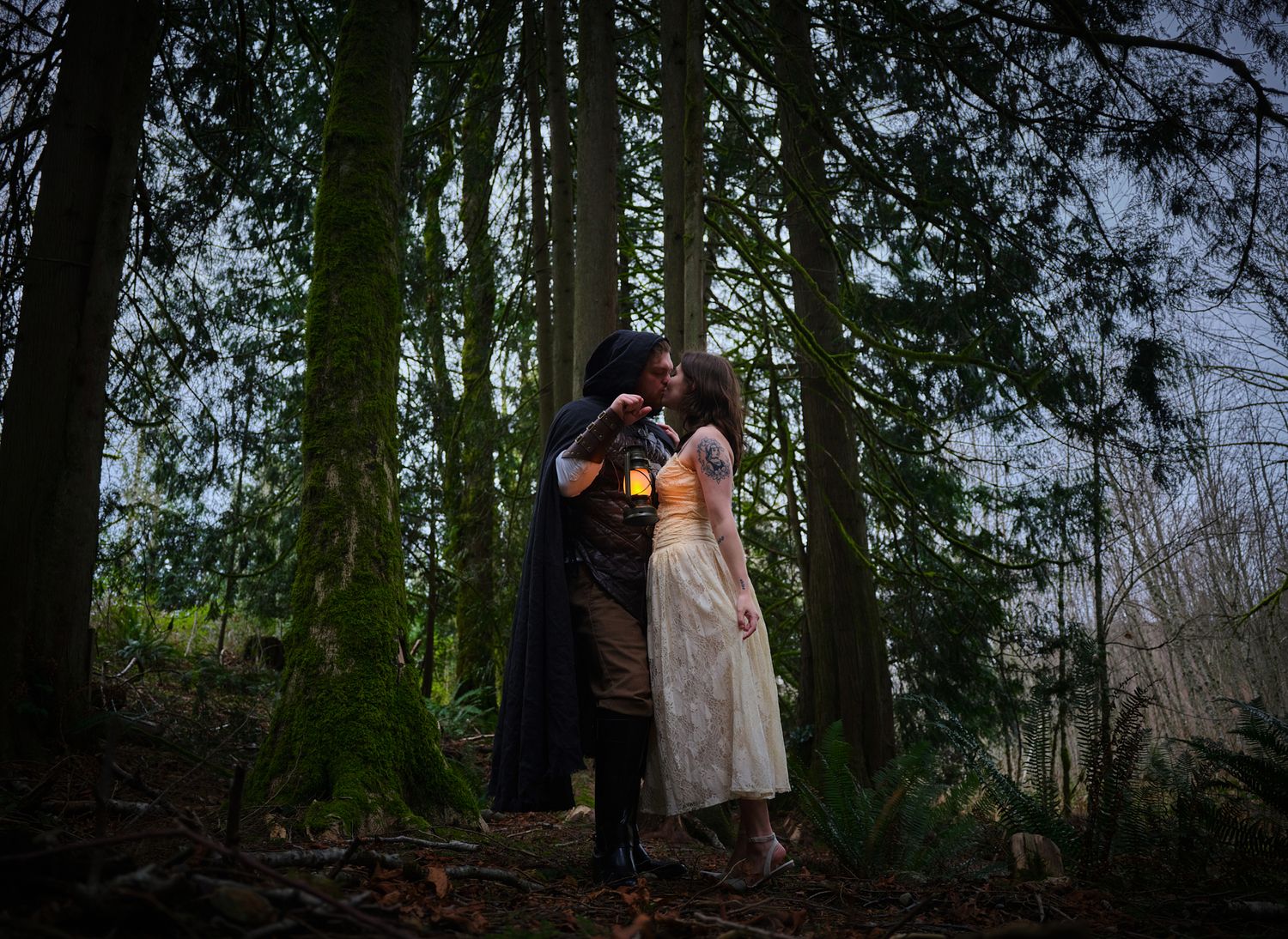 A couple kissing in the woods in Washington State while holding a lantern. Photo by N&D Wedding Photography and Film