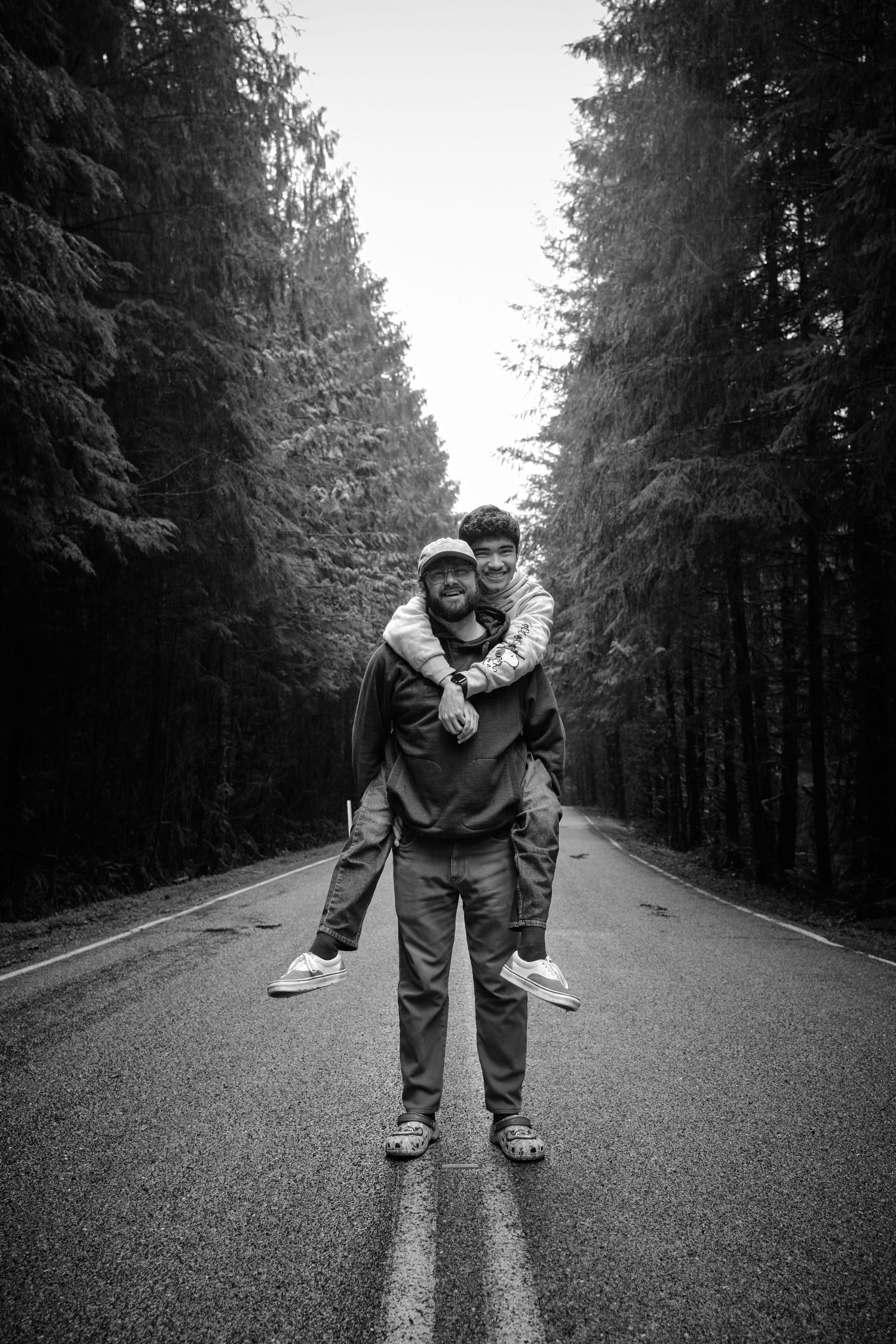 A couple giving a piggyback ride to each other in a WA, State forest in the rain. Photo by N&D Wedding Photography and Film