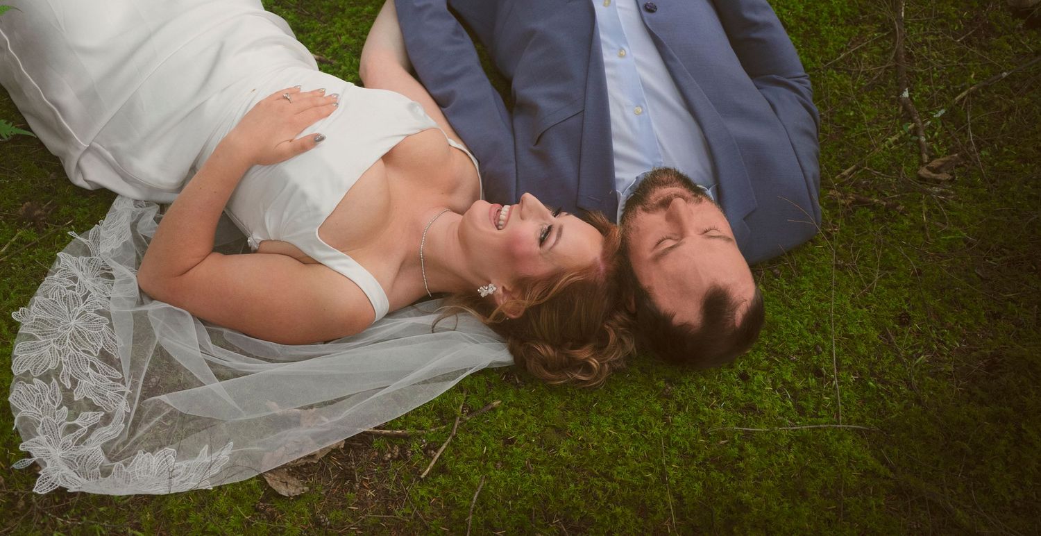A married couple lying on the ground touching their heads together and laughing in WA State. Photo by N&D Wedding Photography and Film