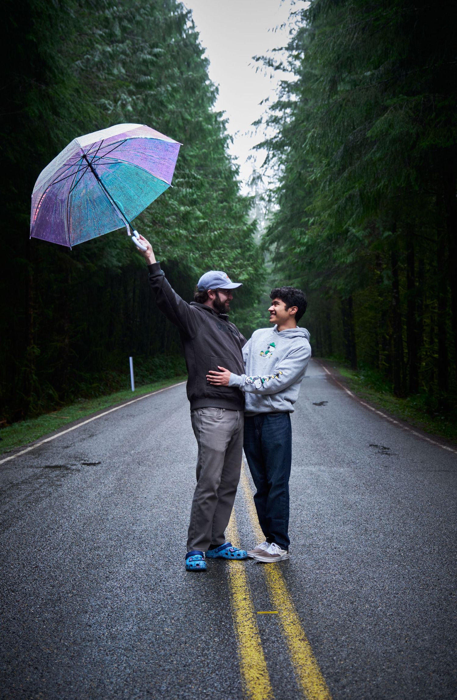 A couple standing in the rain as their umbrella flies away in a WA, State forest in the rain. Photo by N&D Wedding Photography and Film