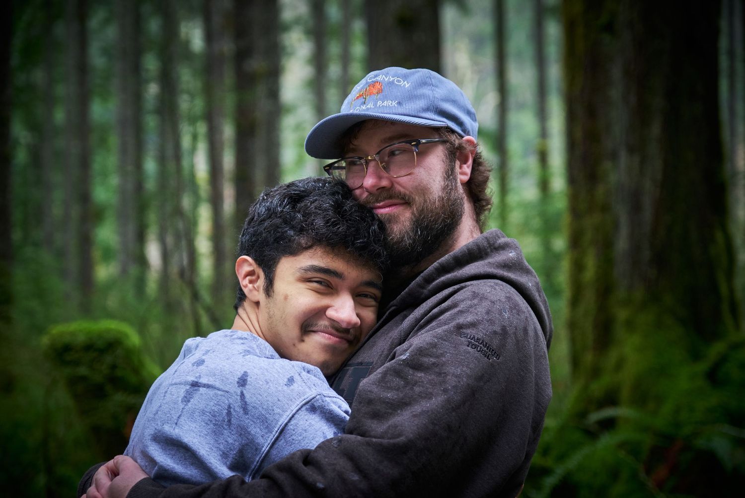 A couple hugging and smiling in a Washington State forest in the rain. Photo by N&D Wedding Photography and Film