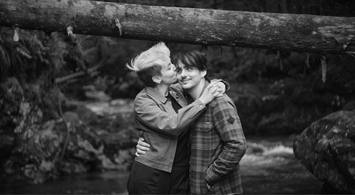 A couple kissing near a river in a forest in Washington State. Photo by N&D Wedding Photography and Film