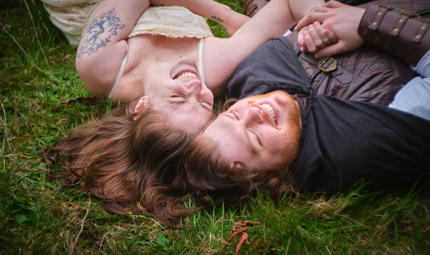 A couple laying in the grass with their heads touching. Taken in Washington State forest. Photo by N&D Wedding Photography and Film
