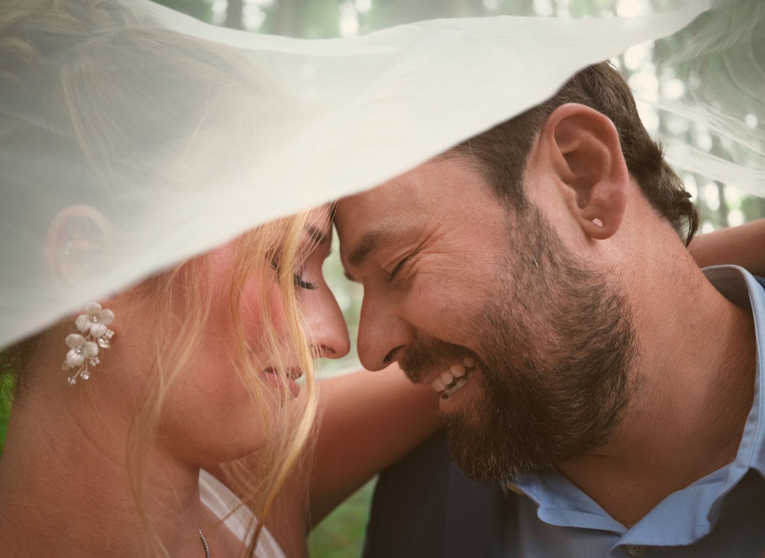A married couple leaning their heads close together under the bride's veil in a WA State forest. Photo by N&D Wedding Photography and Film