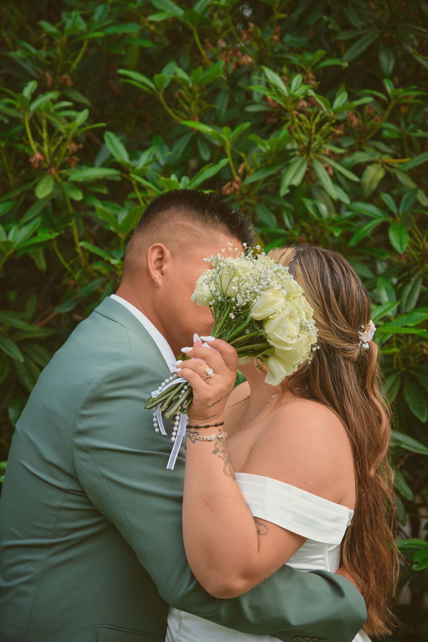 Newlyweds kissing behind the bouquet near some bushes in Tulalip Washington. Photo by N&D Wedding Photography and Film
