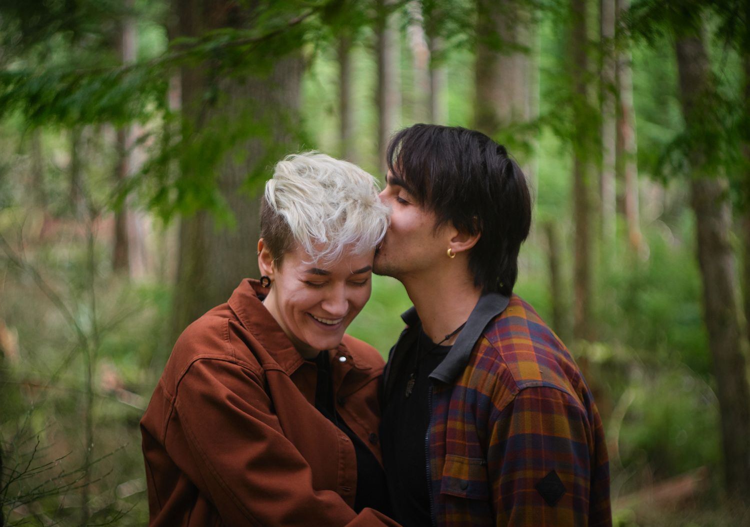 A couple kissing and giggling in a dense forest in Washington State. Photo by N&D Wedding Photography and Film