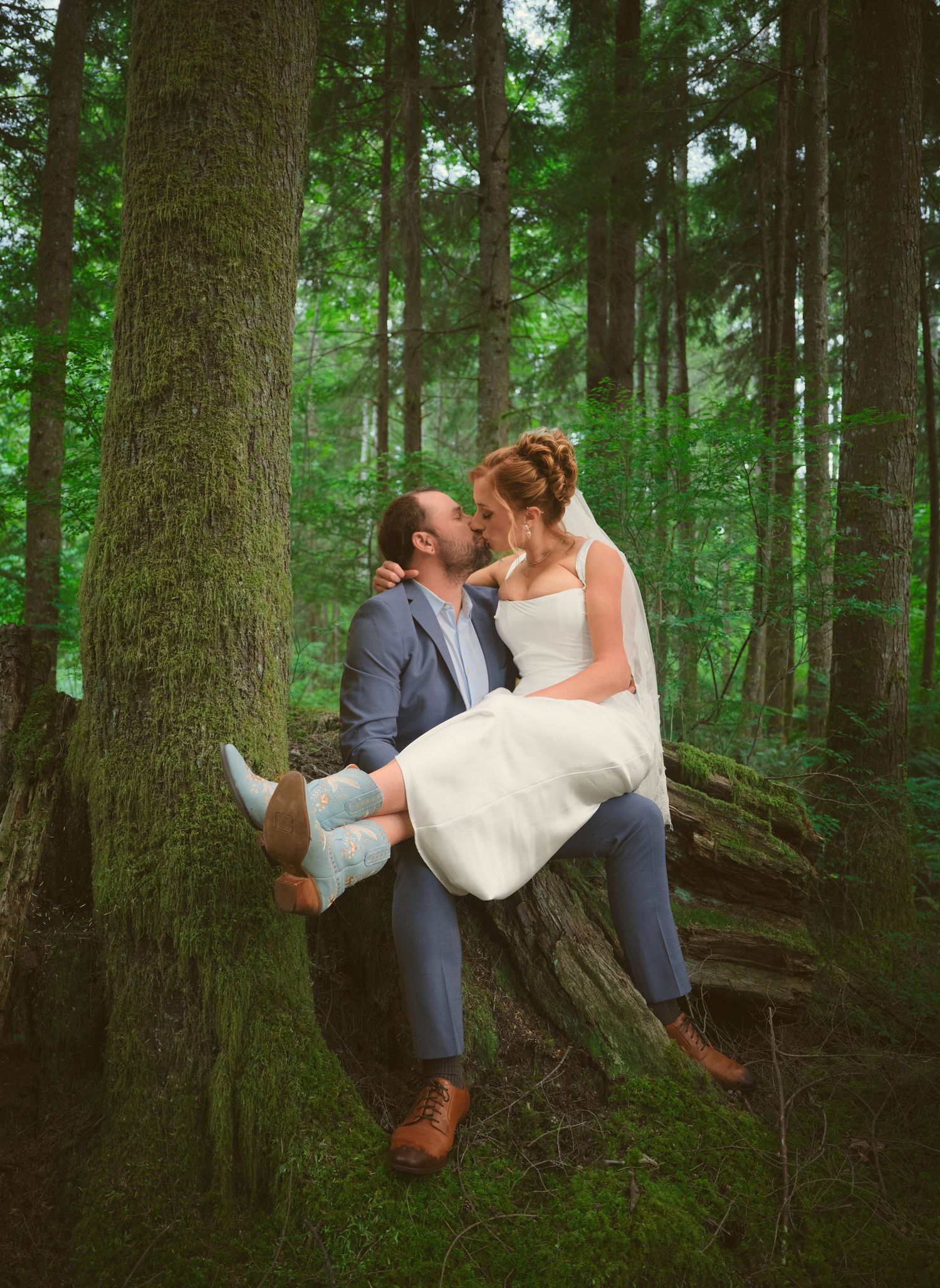 A photo in the WA State woods of a married couple kissing and the bride is in the groom's lap . Photo by N&D Wedding Photography and Film