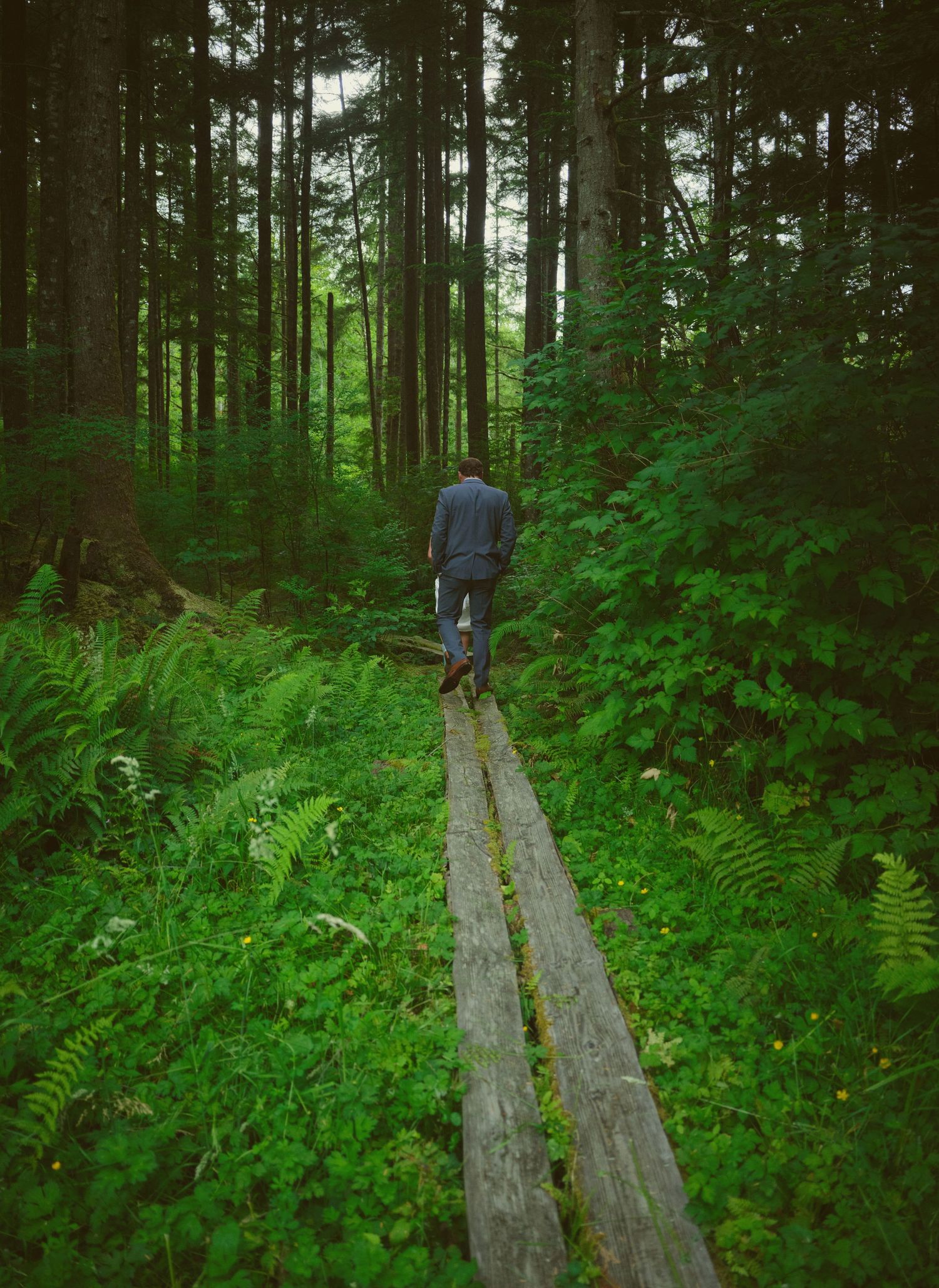 A groom being led through the WA State woods by his new bride, she is mostly not visible. Photo by N&D Wedding Photography and Film