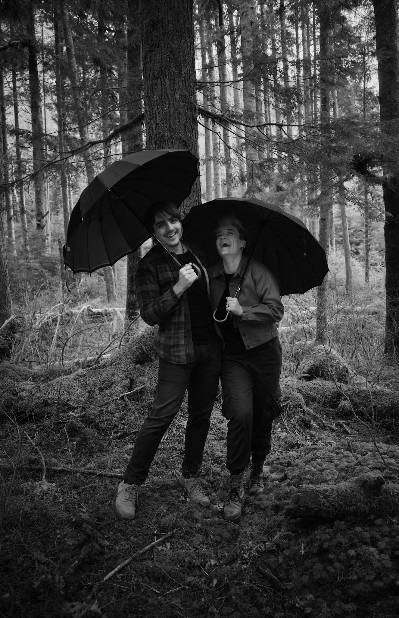A couple laughing hard while holding umbrellas in a forest in Washington State. Photo by N&D Wedding Photography and Film