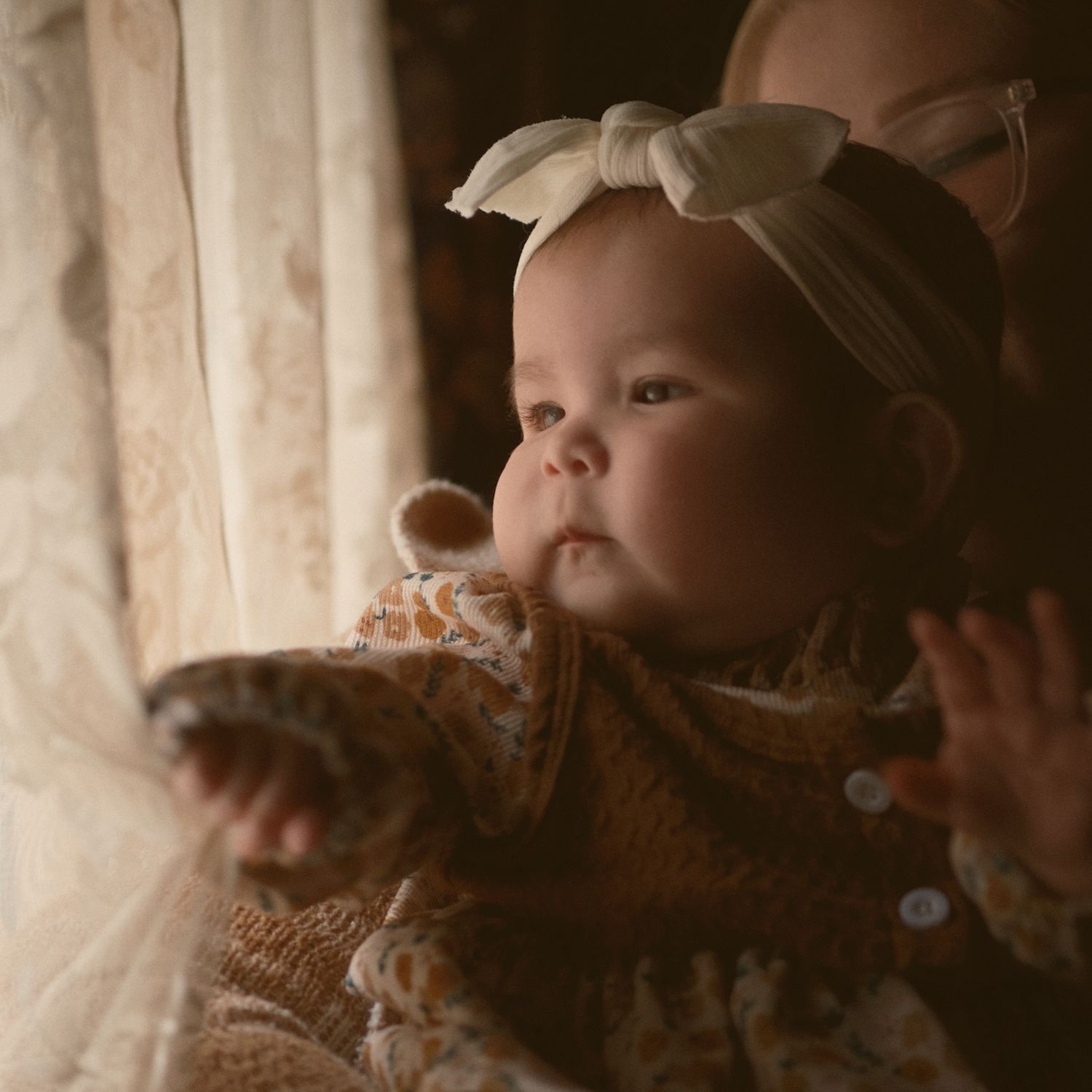 A baby pulling the window curtain to see outside, taken in Snohomish County, Washington State. Photo by N&D Wedding Photography and Film