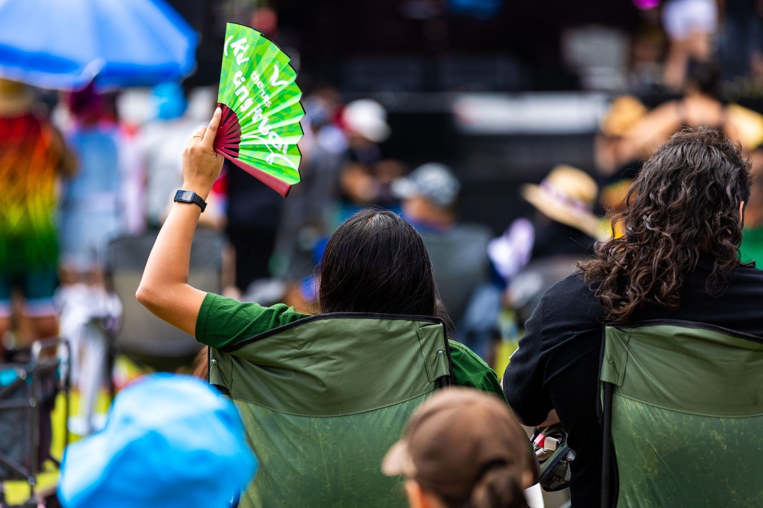 Crowd of attendees wave green folding fans during outdoor summer event.
