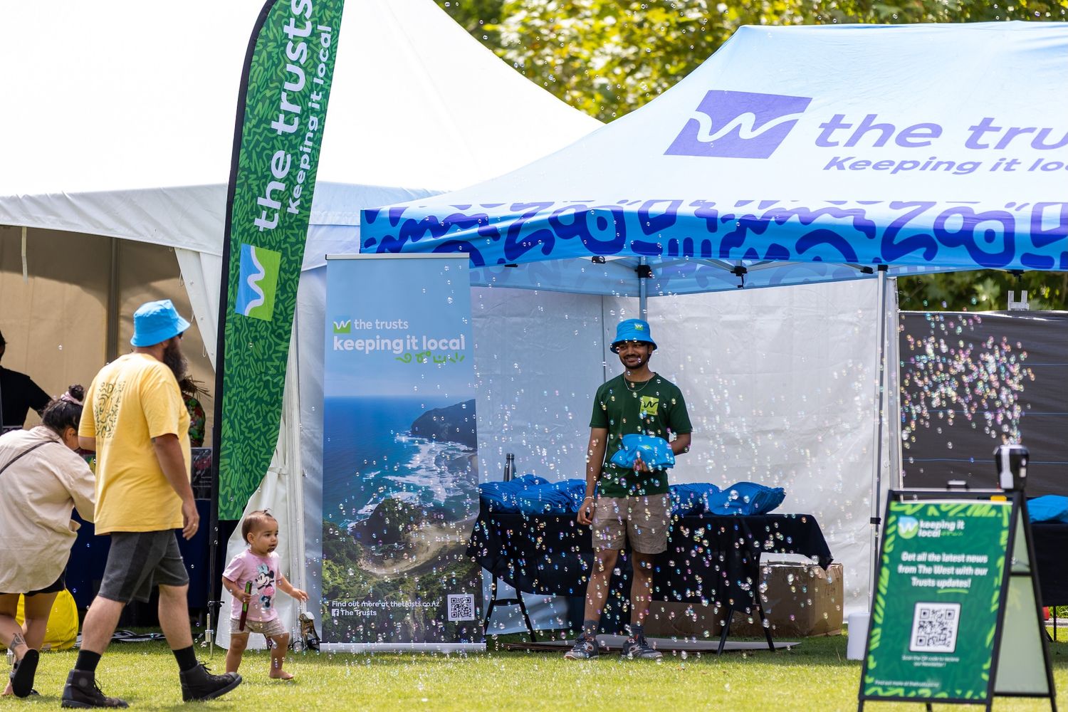 Event banners and signage displayed against green trees at an outdoor gathering.