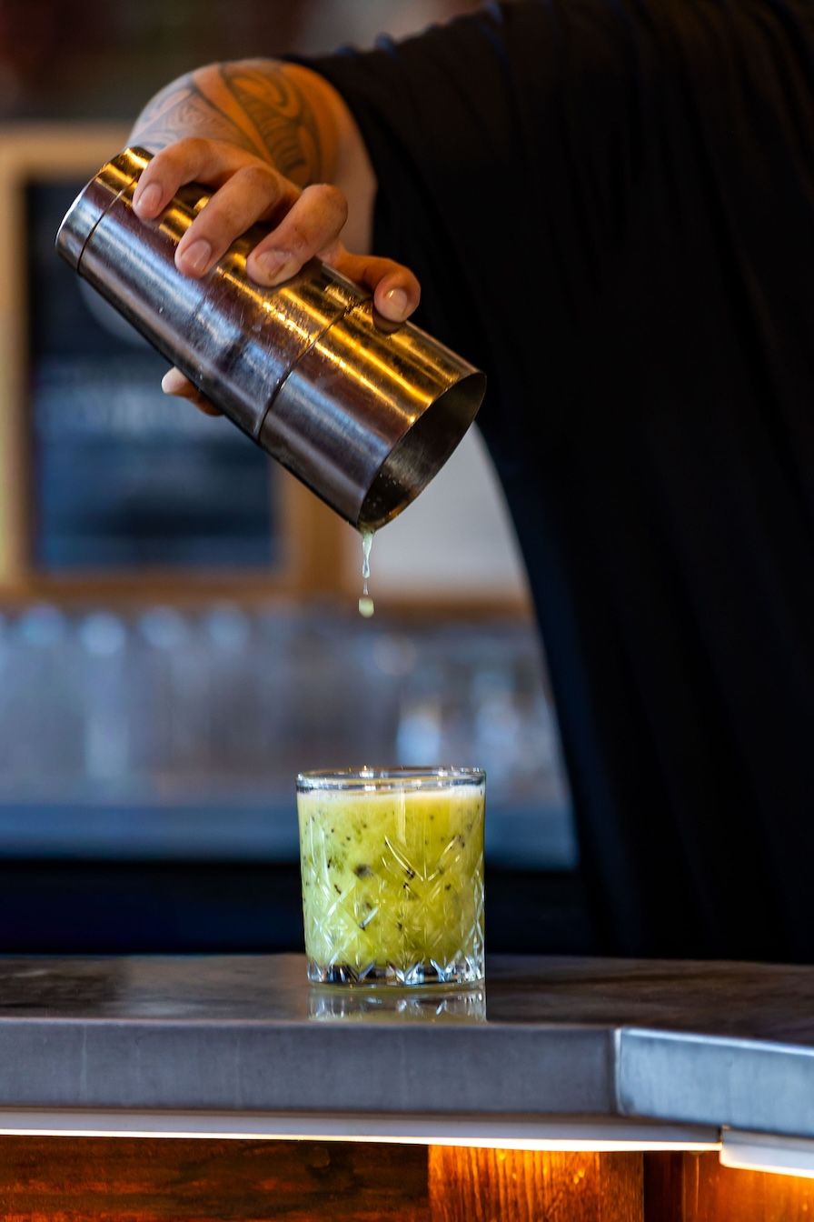A bartender pours a vibrant green cocktail into a rocks glass in a sequence of four progressive shots.