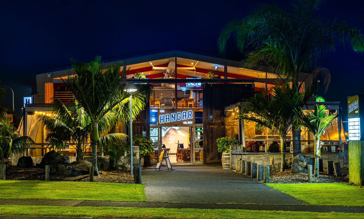 Panoramic nighttime view of an illuminated resort building with palm trees and tropical landscaping in the foreground.